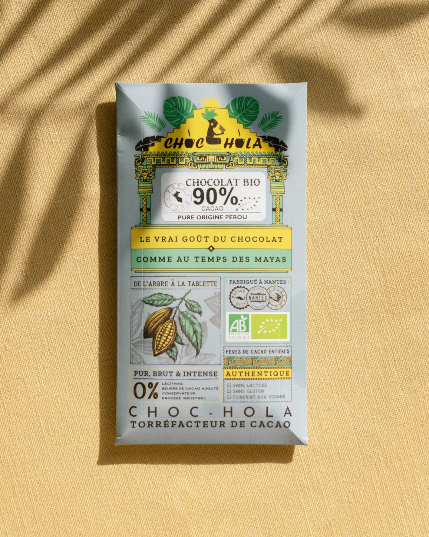 Packaging d'un chocolat bio à 90% de cacao, avec des illustrations de feuilles de cacao et de plantes, des labels bio européens, et des indications sur le produit comme 'authentique', sans lactose, sans gluten, et vegan.