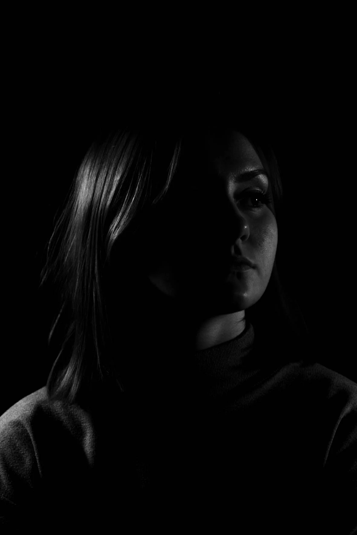 Portrait en noir et blanc d'une femme dont le visage est partiellement dans l'ombre, avec un calme expression.