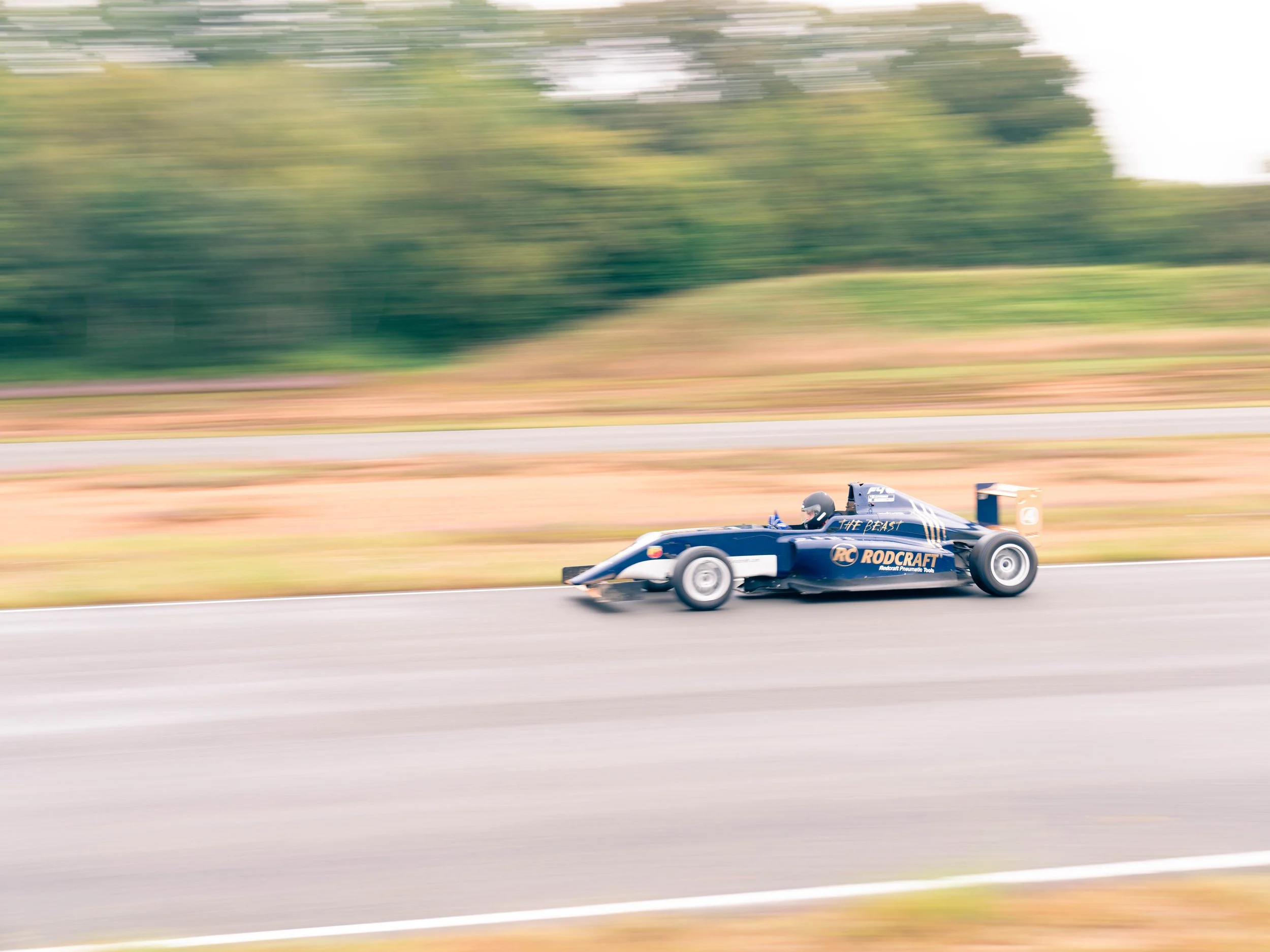 Voiture de course en mouvement sur une piste, arrière-plan flou, pilote portant casque.