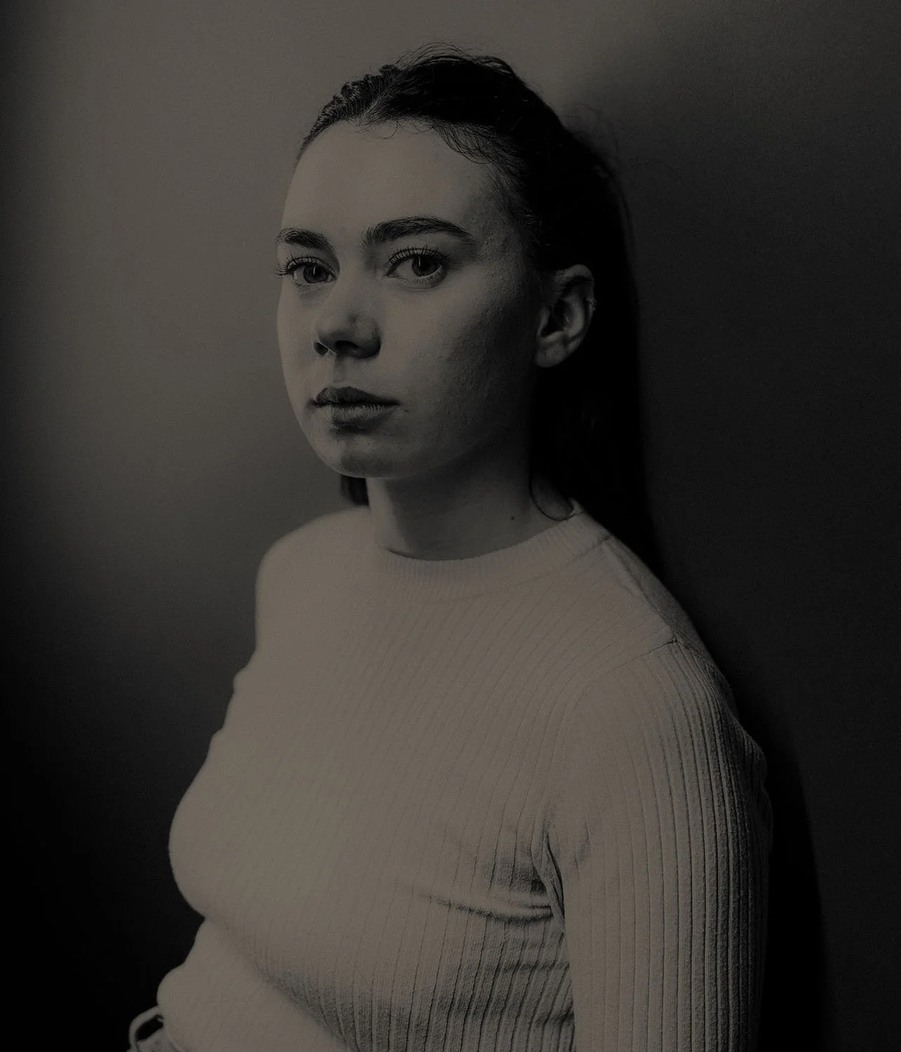 Portrait en noir et blanc de Juliette Ayoul regardant vers l'avant, portant un pull côtelé, avec un fond sombre.