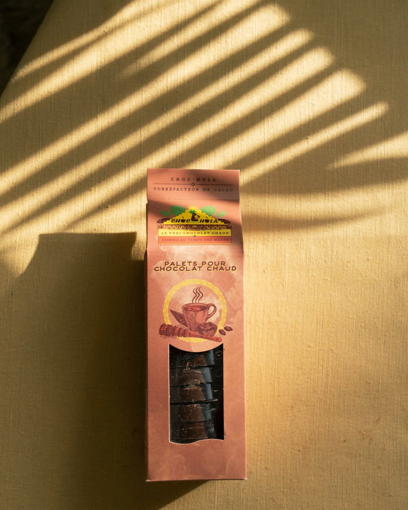 Une boîte de bâtons pour chocolat chaud. La boîte est rose avec une illustration d'une tasse de chocolat chaud, des grains de café et une tige de cacao.