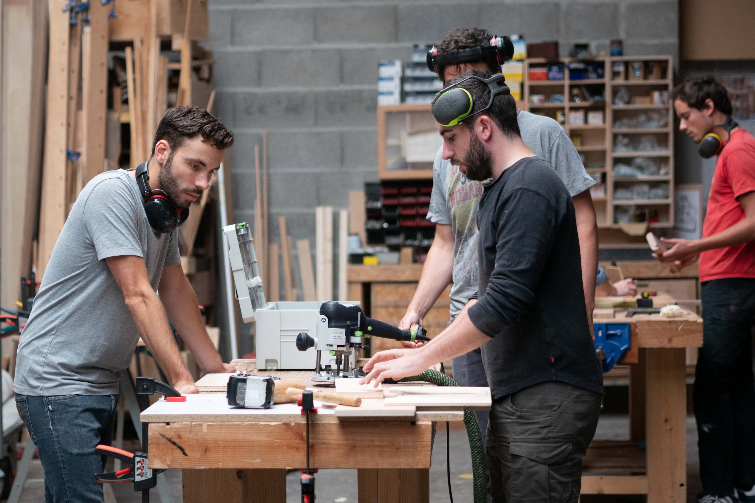 Groupe de jeunes travaillant dans un atelier de menuiserie, utilisant une machine-outil pour couper du bois.