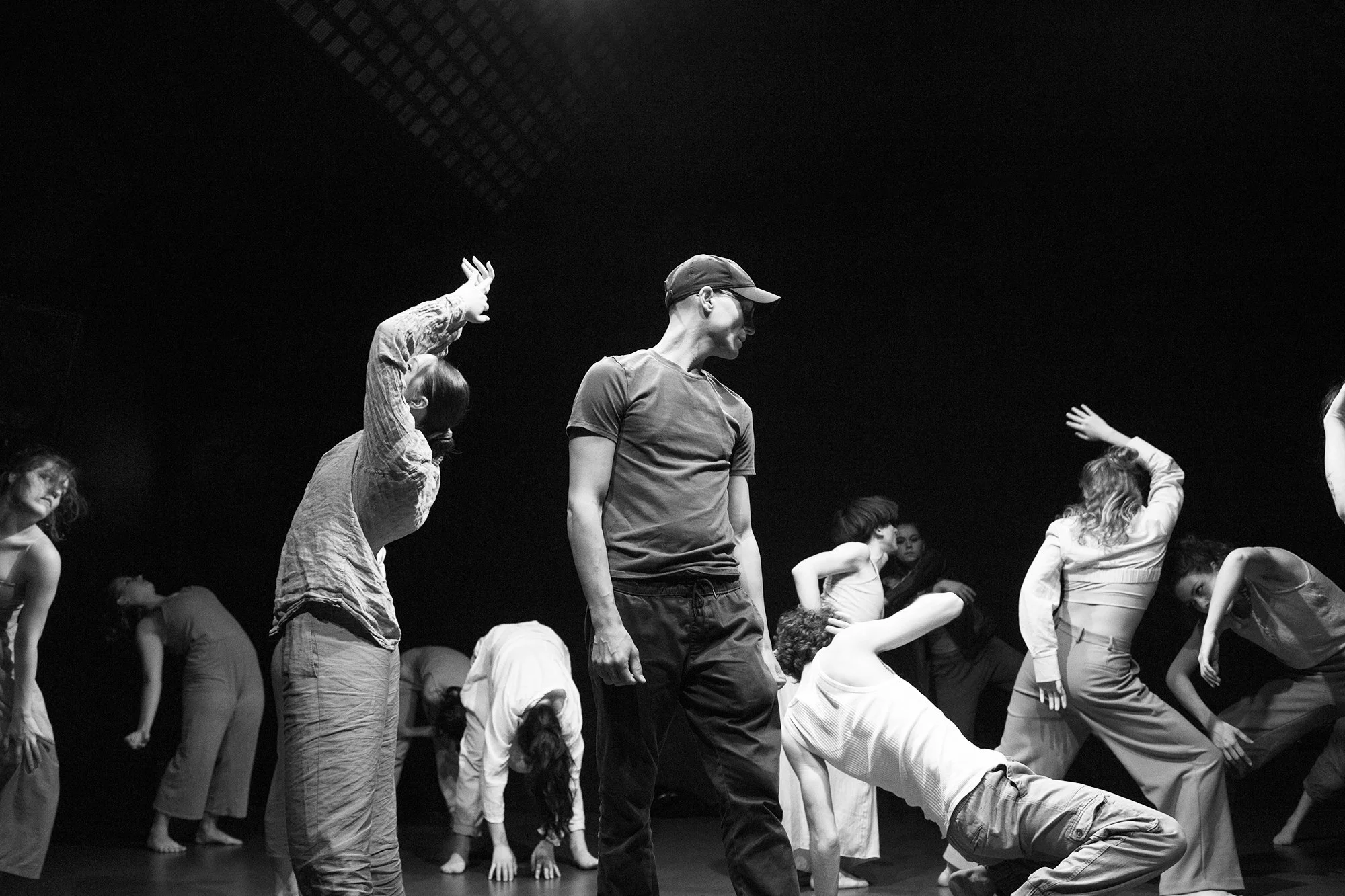 Groupe de personnes en train de pratiquer la danse ou le yoga sur scène, certains en position de flexion ou d'étirement, dans une ambiance concentrée.