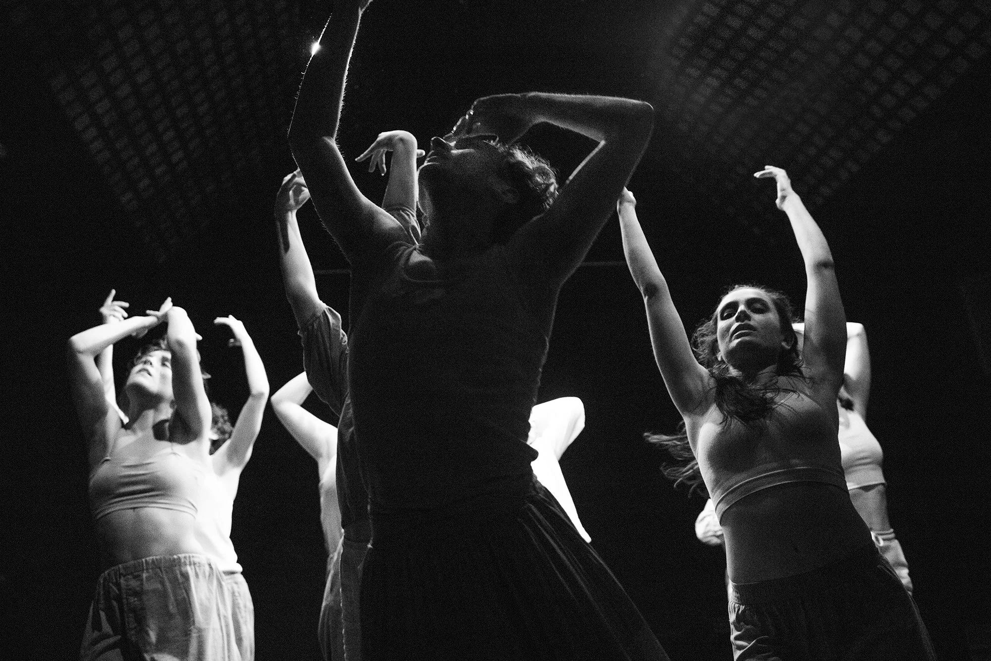 Groupe de danseurs en mouvement dans une salle de danse, éclairage tamisé, photographie en noir et blanc.