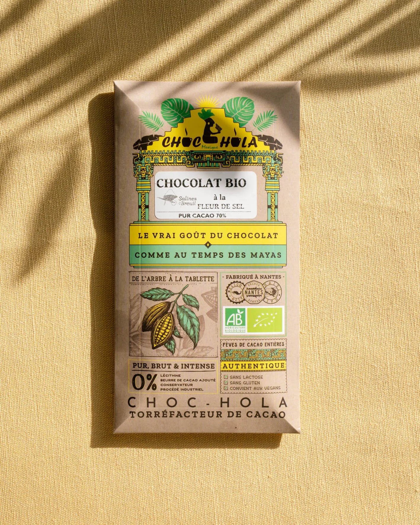 Emballage de chocolat bio à la fleur de sel, avec un design mexicain, un dessin de fève de cacao, et des labels biologiques, sur un fond en tissu beige.