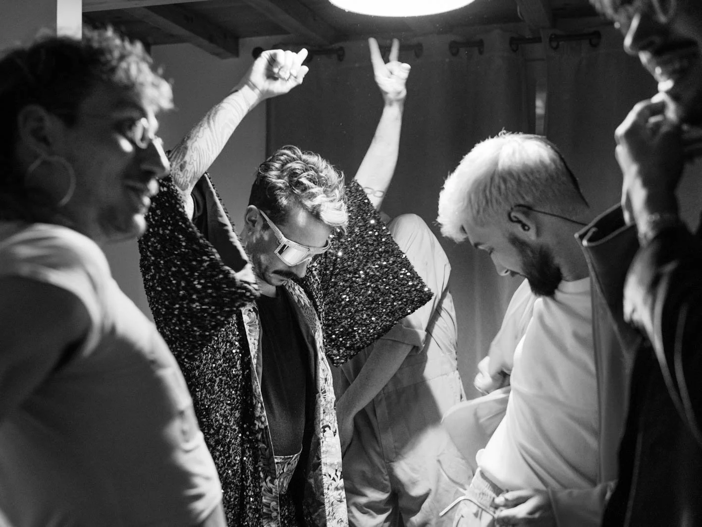 Groupe de cinq personnes joyeuses dans une pièce, dont deux femmes et trois hommes, avec une ambiance de fête ou de célébration, tout en étant en noir et blanc.