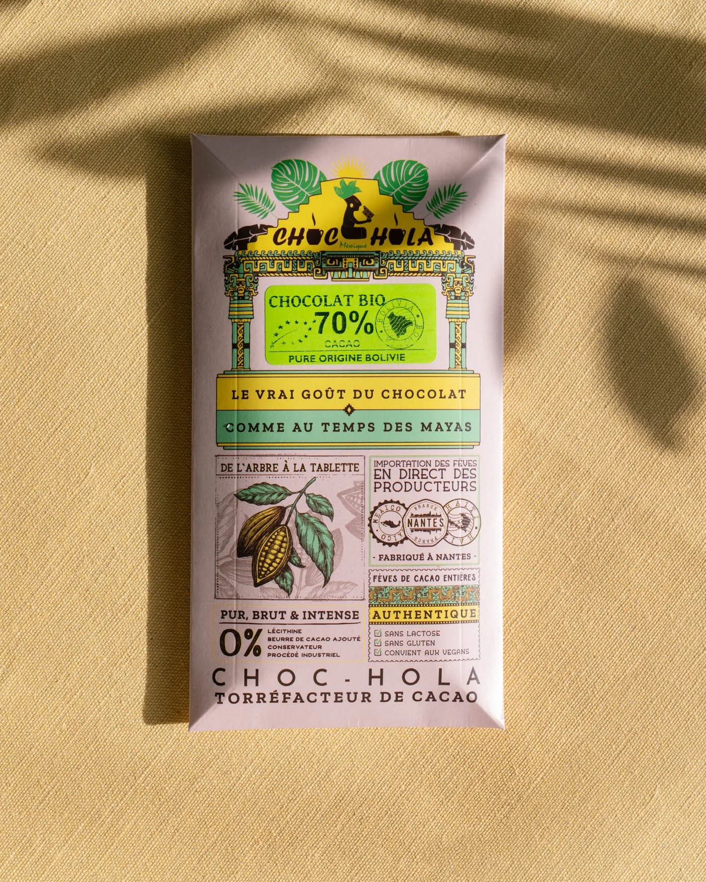 Pâte de chocolat bio à 70% de cacao, d'origine bolivienne, avec un design coloré évoquant la culture maya, sur un fond en tissu beige.