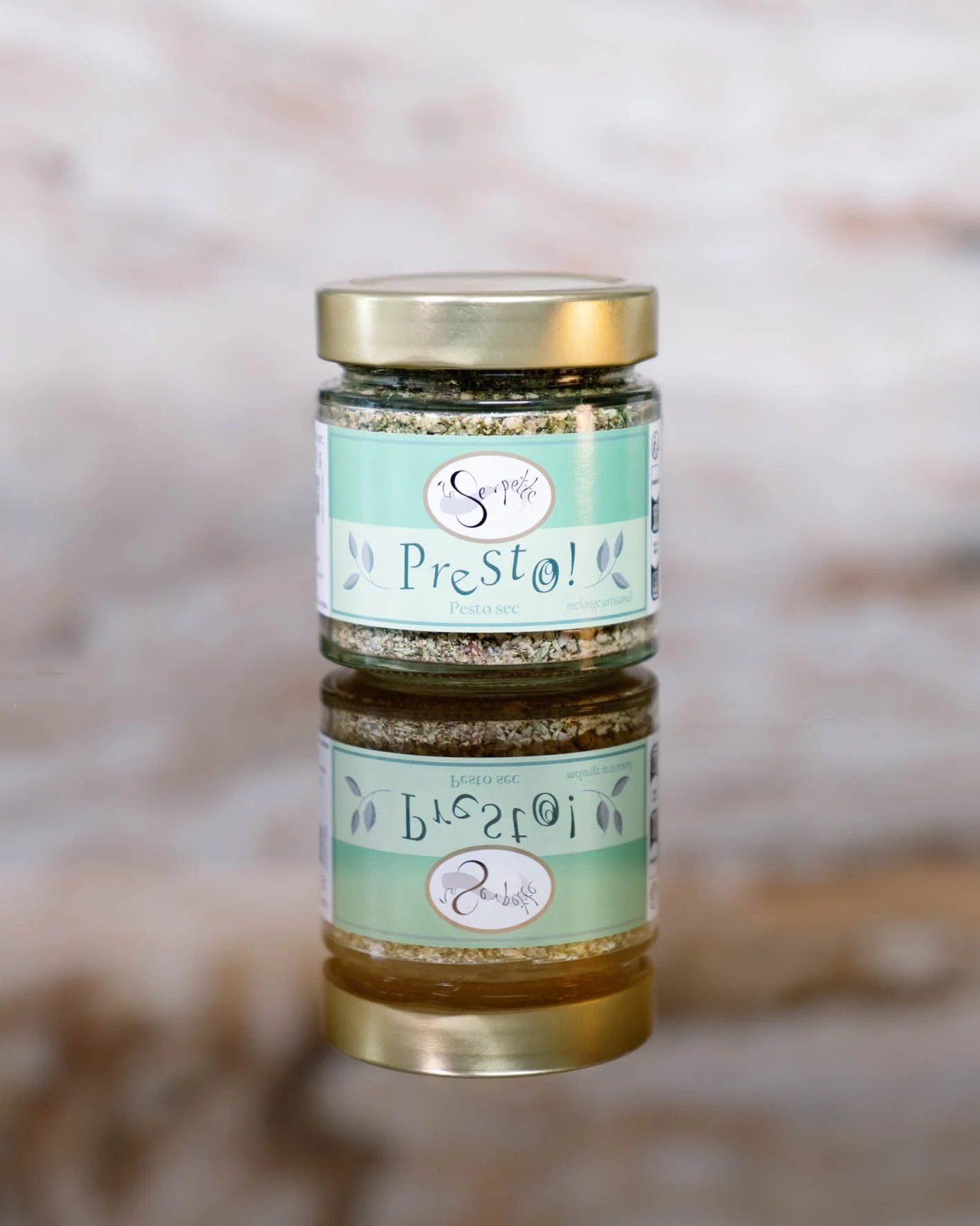 Un pot en verre de pesto sec avec un couvercle doré, posé sur une surface en bois. Le pot a une étiquette verte avec la marque 'Le Sépétile' et le nom 'Presto!'.