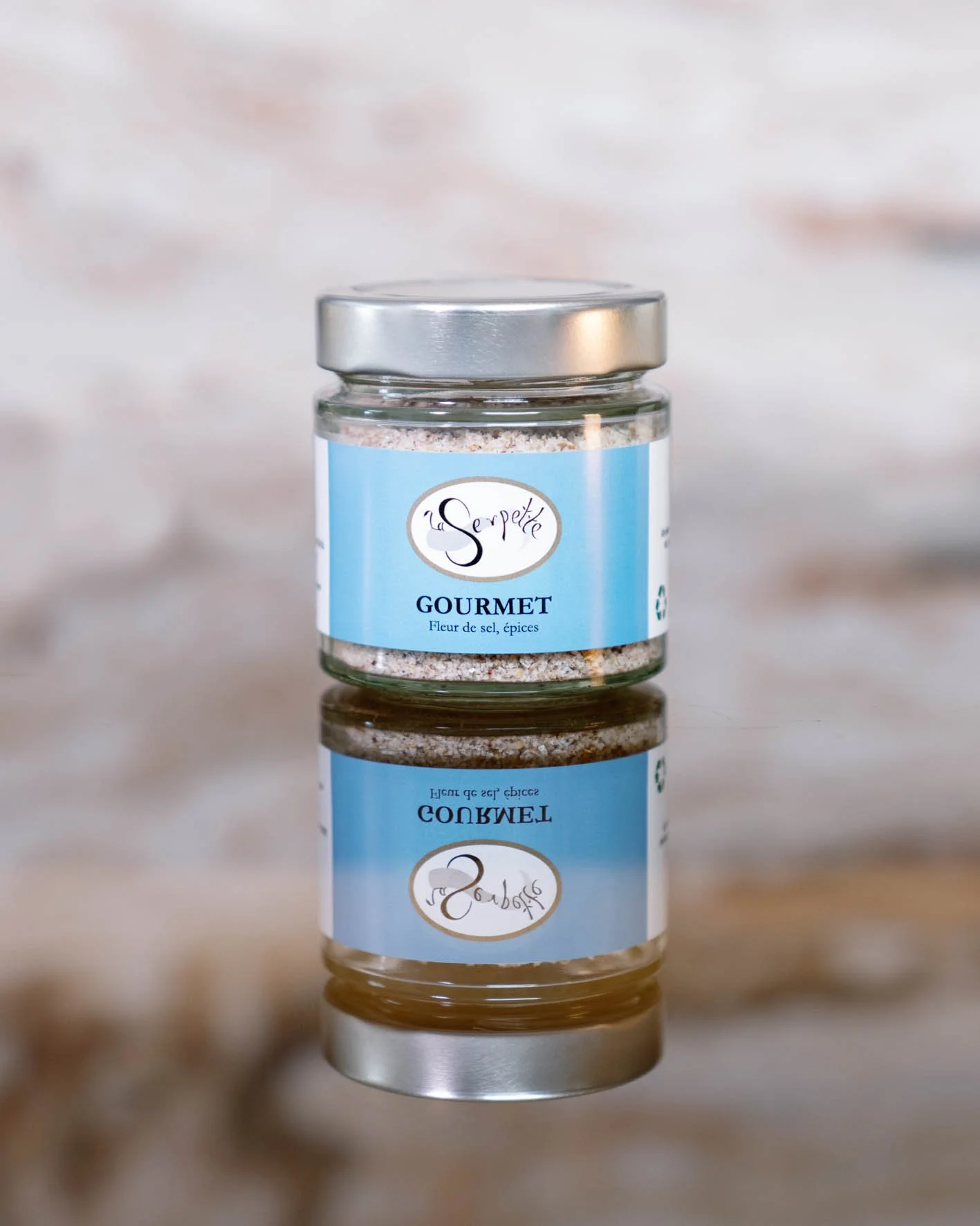 Pot en verre avec un couvercle métallique contenant un mélange d'épices, étiquette bleue avec le texte "la Serpette GOURMET Fleuri de sel, épices".