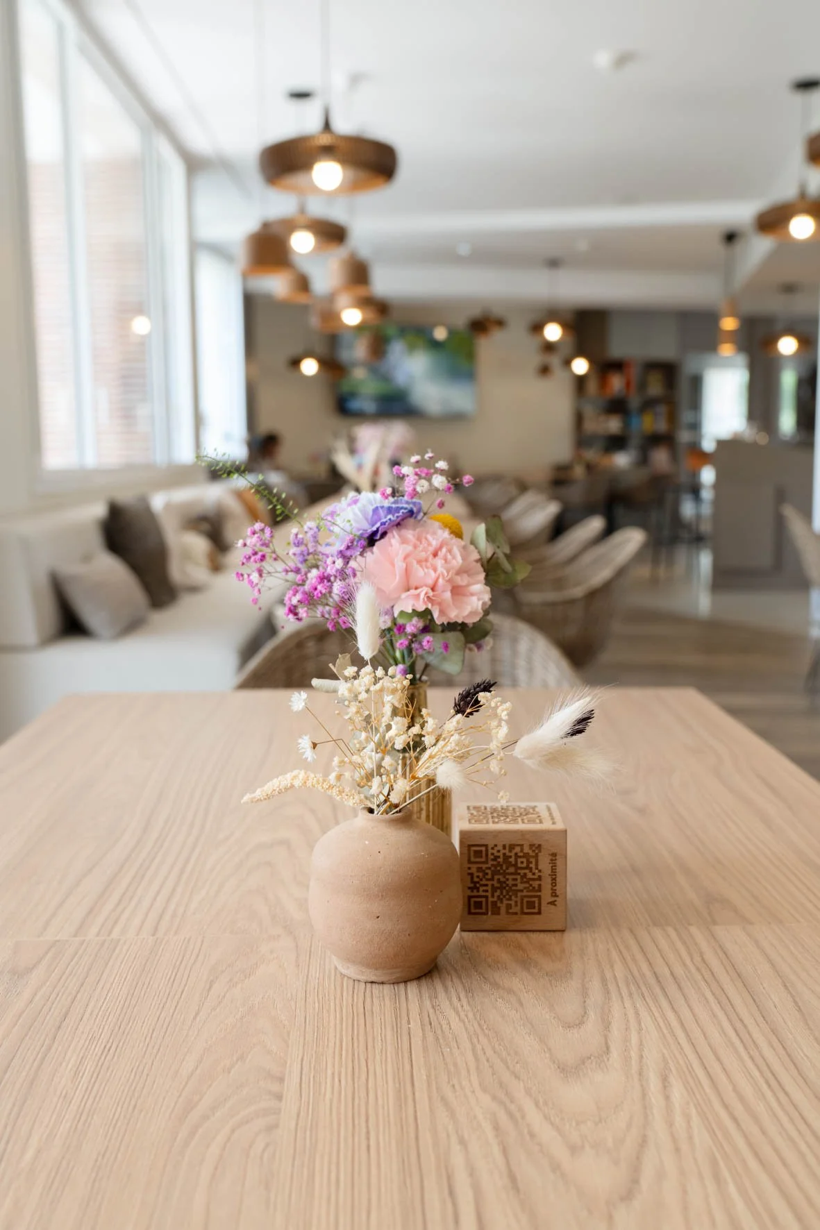 Vase en terre cuite avec bouquet de fleurs colorées sur une table en bois dans un café ou restaurant modern.