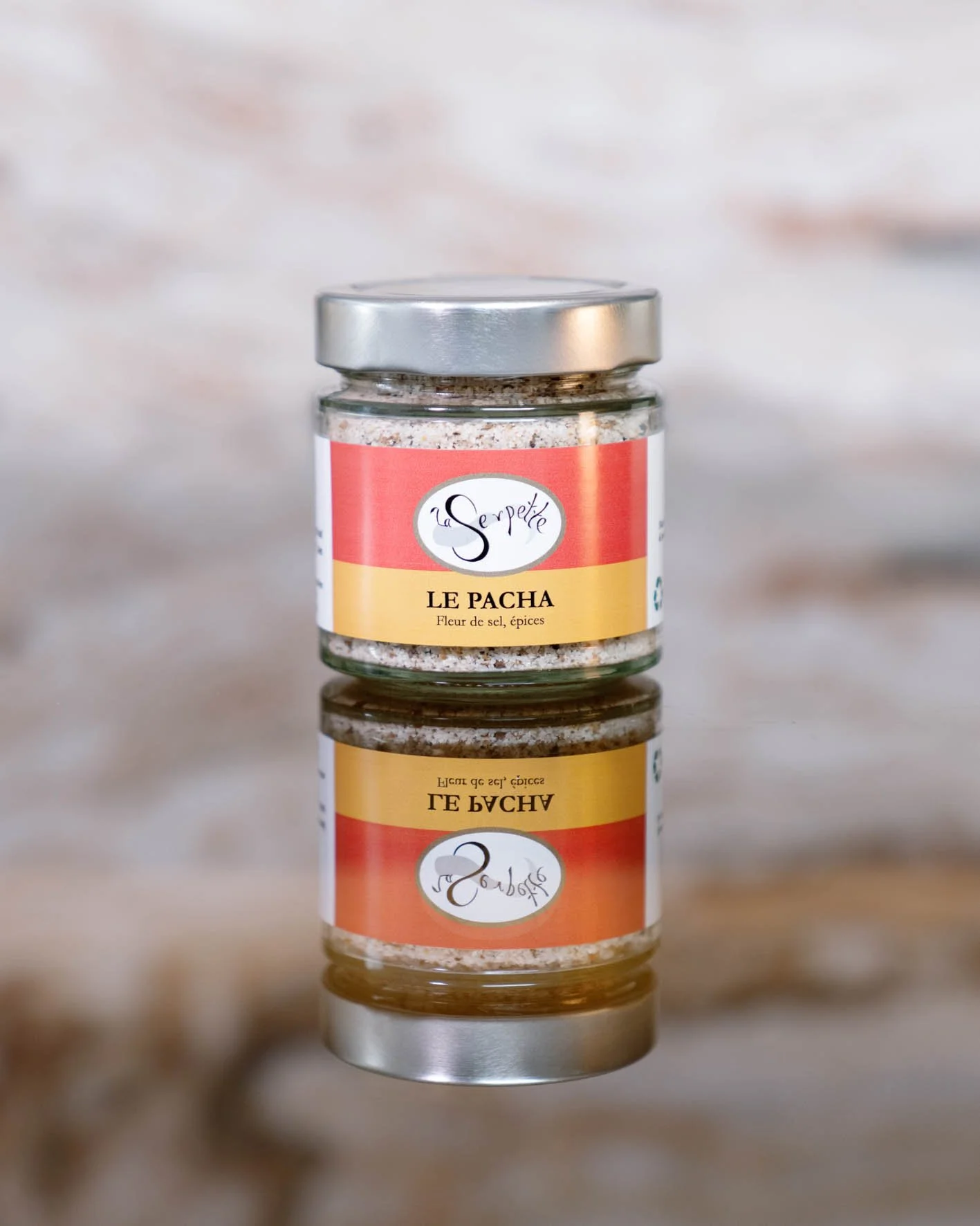 Pot en verre avec un ruban rouge-orange, contenant un mélange de sel épicé, marqué 'la Serpette' et 'LE PACHA'.