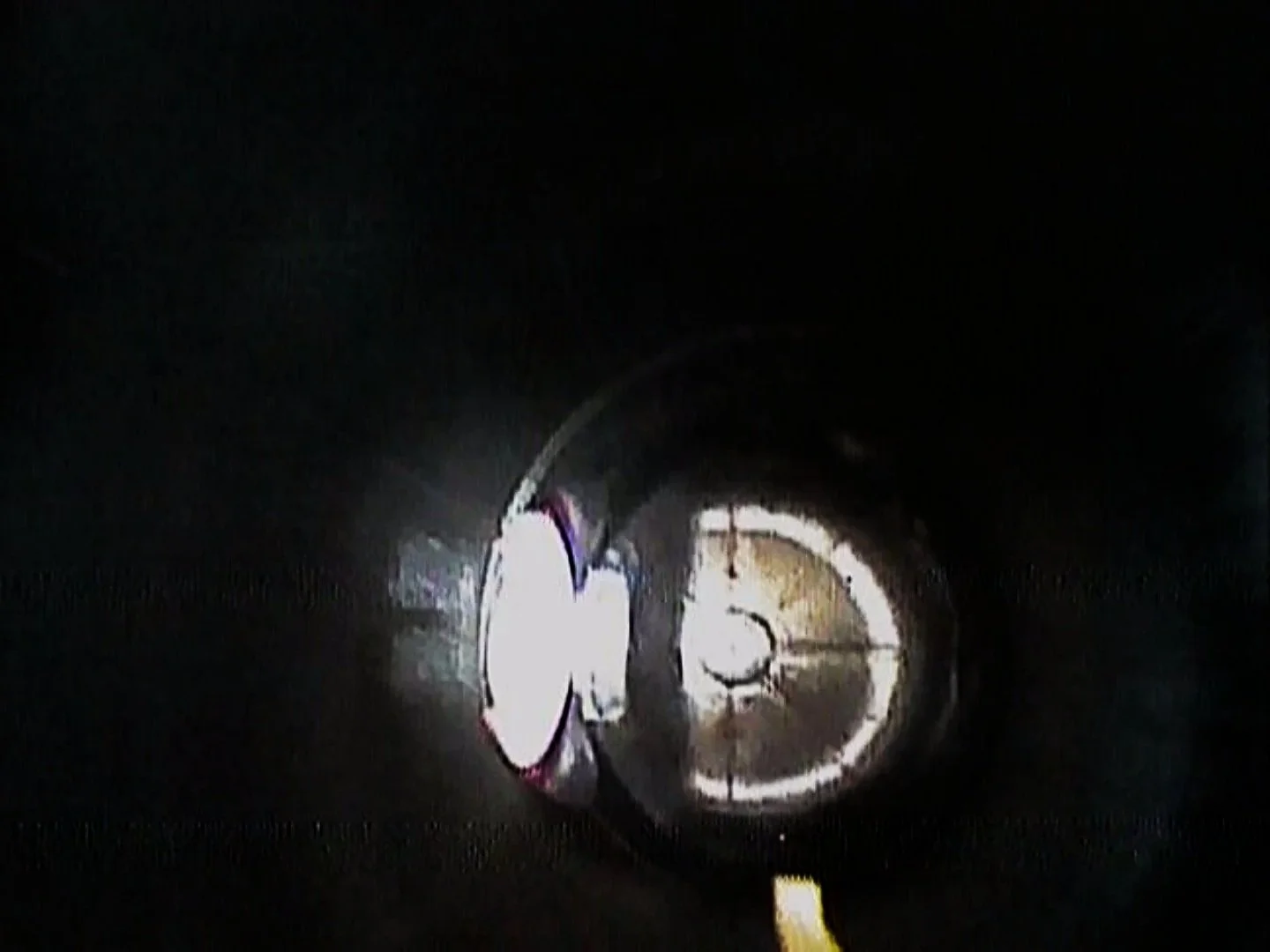 A person in protective gear working inside a dark, enclosed space with a circular pipe or tunnel being illuminated.