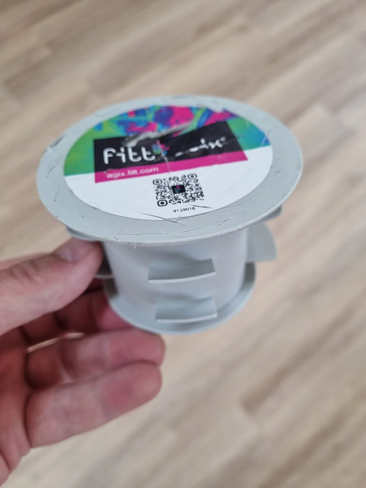 A hand holding a small white container with a colorful, holographic label on top that reads 'fittix' and includes QR codes and a website URL.