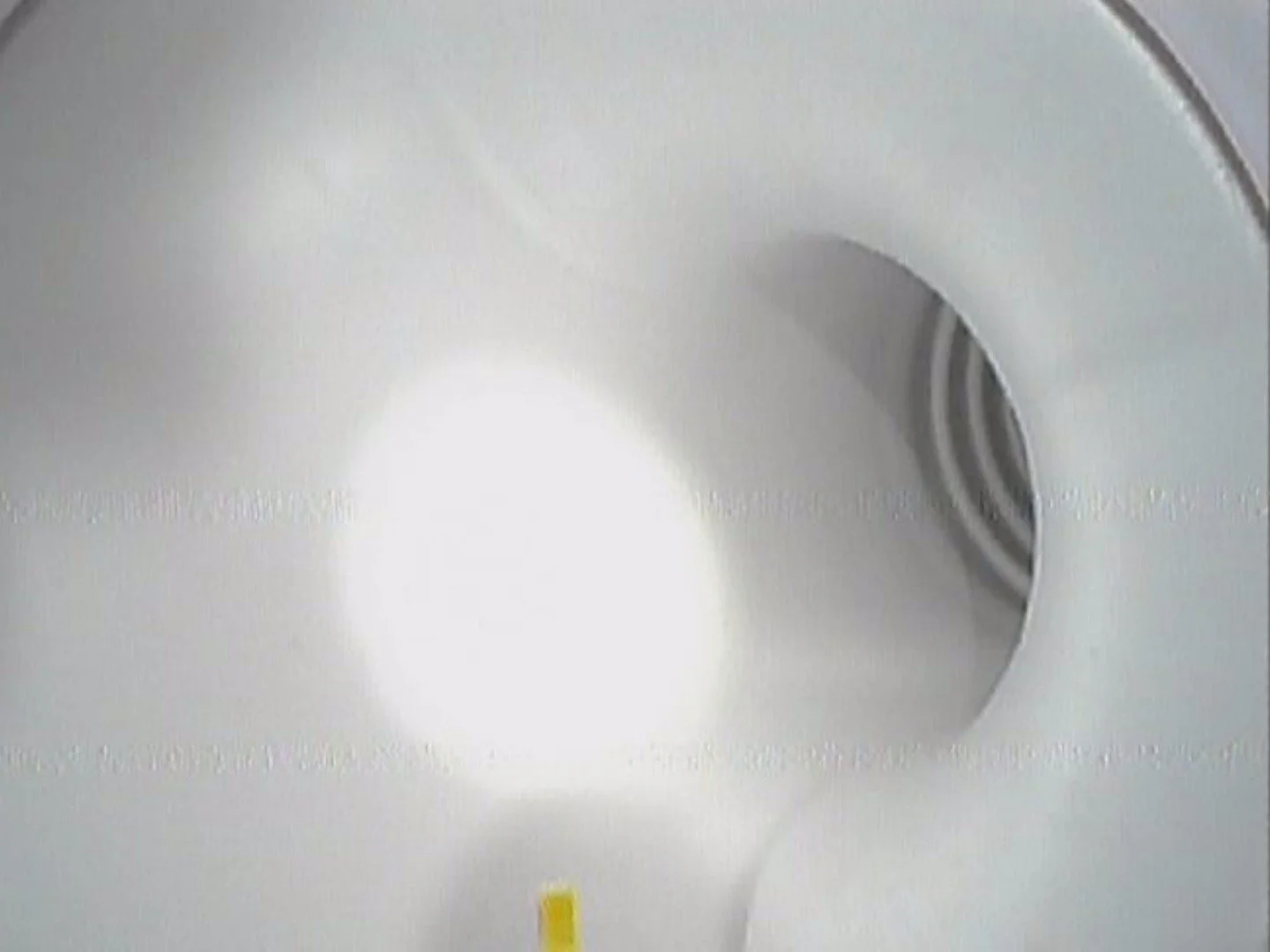 Close-up of a white toilet bowl with the seat lifted, showing the interior and vent fan on the wall behind it.