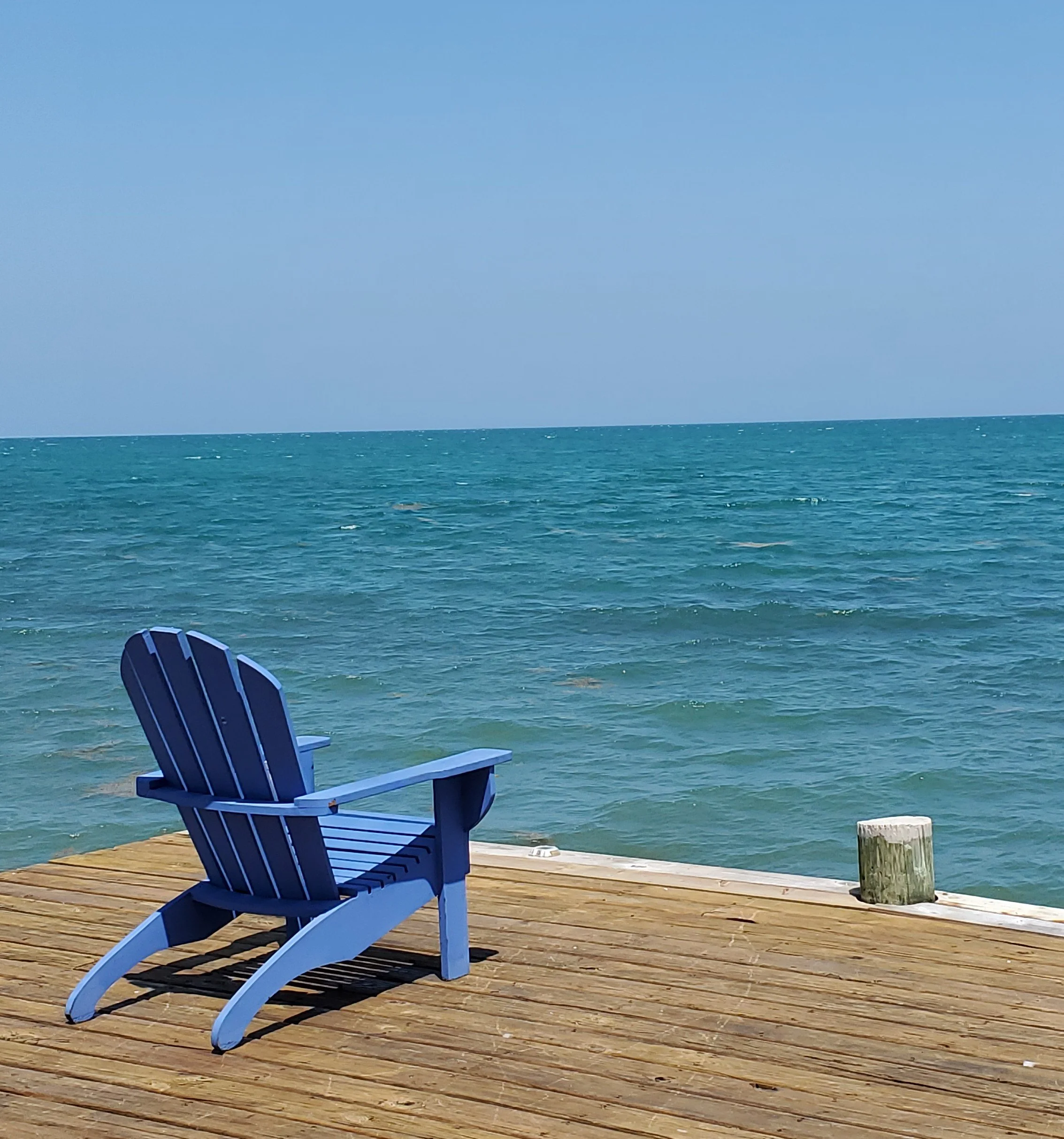 Contemplative photo by Gretchen Martens  of an adirondack chair on a dock overlooking the Caribbean Sea