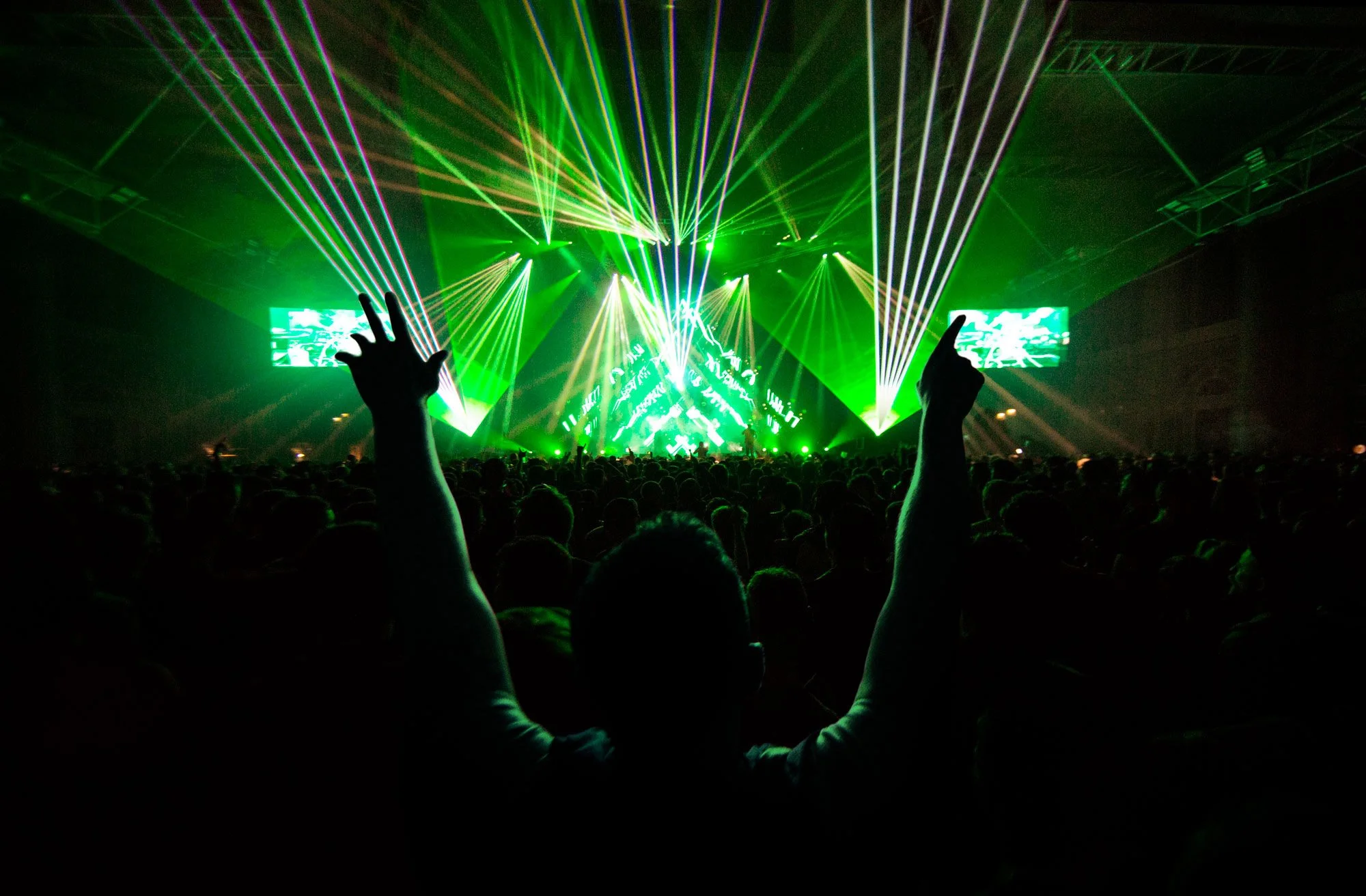 Andy C Alexandra Palace, green laser lights projecting in different directions, with a crowd of people raising their hands and watching the stage.