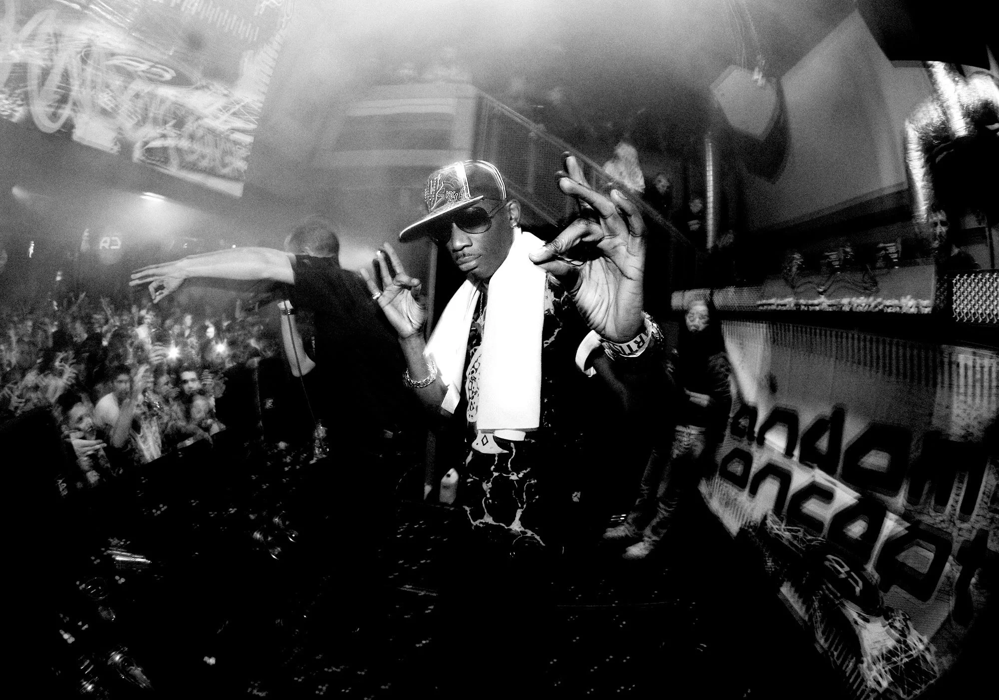 MC Skibadee in a crowded nightclub or concert venue with bright lights and a cheering crowd.