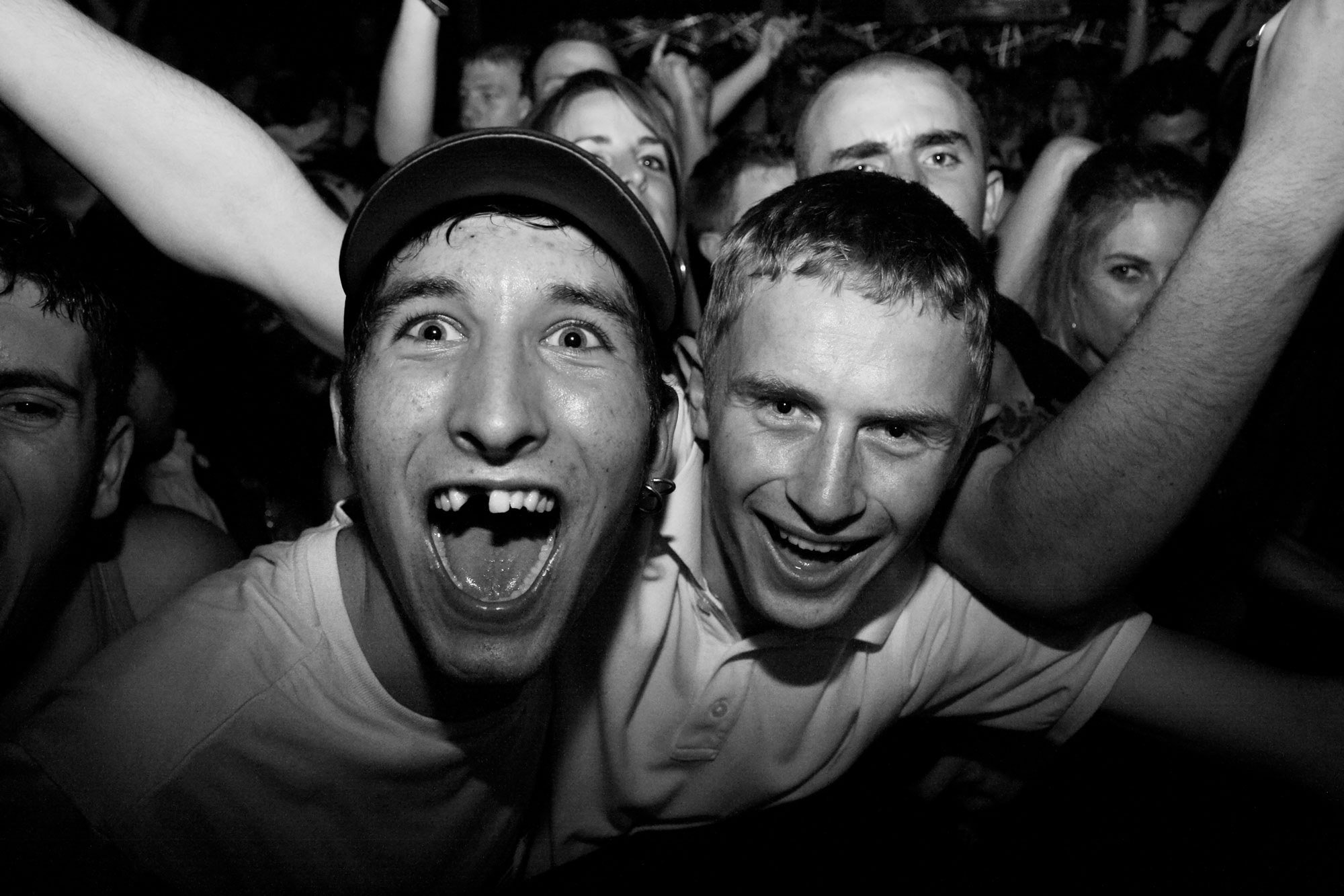 Group of people at a party, with two young men in the front smiling and making excitement expressions, surrounded by friends in a lively atmosphere.