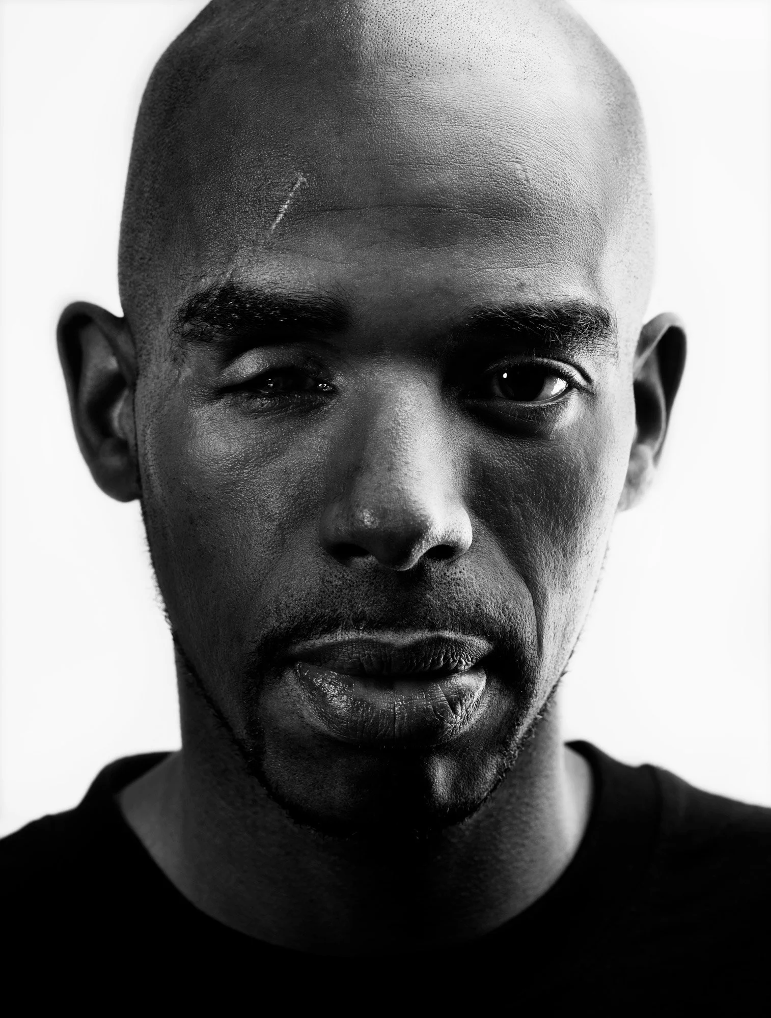 Close-up black and white portrait of a man with a shaved head and a beard, wearing a dark shirt.