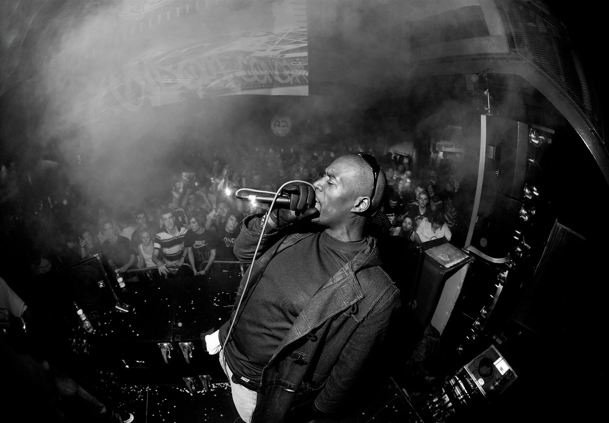 A male performer singing into a microphone on stage with a crowd of people watching in front.