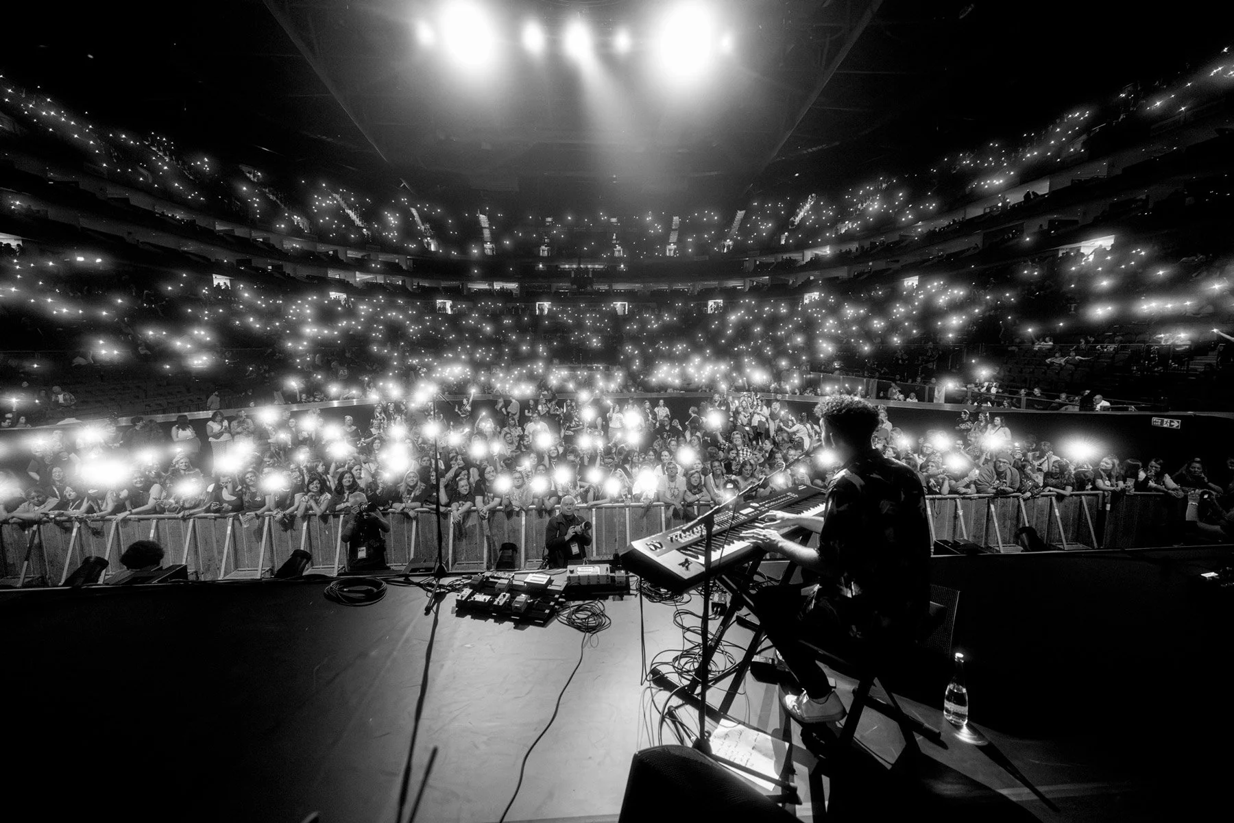 Billy Lockett playing keyboard on stage at the O2 London, the audience holding up lit phones creating a starry effect in the background.