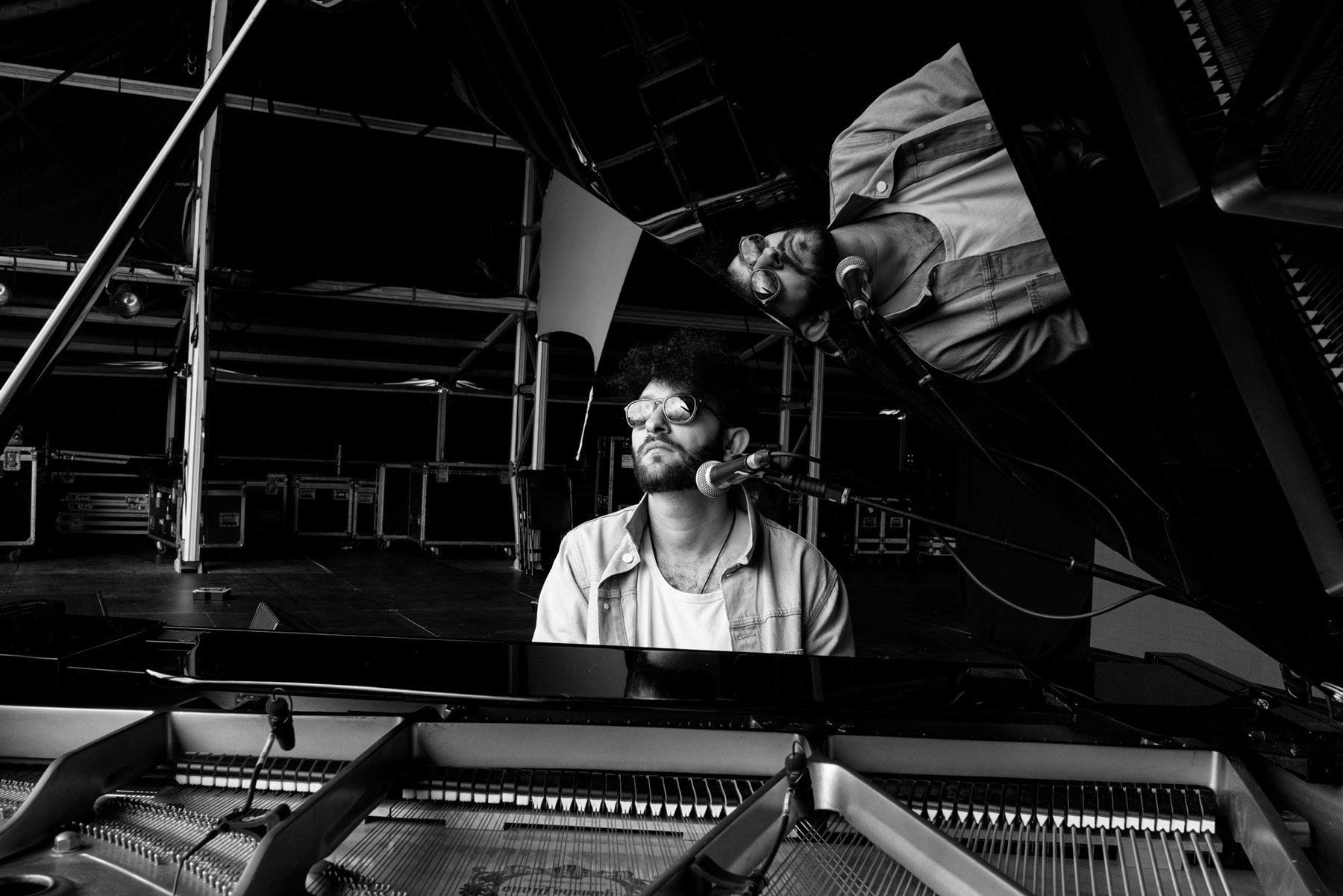 Billy Lockett playing a grand piano, with one at the keyboard and the other possibly singing or speaking into a microphone in a large stage or studio setting.