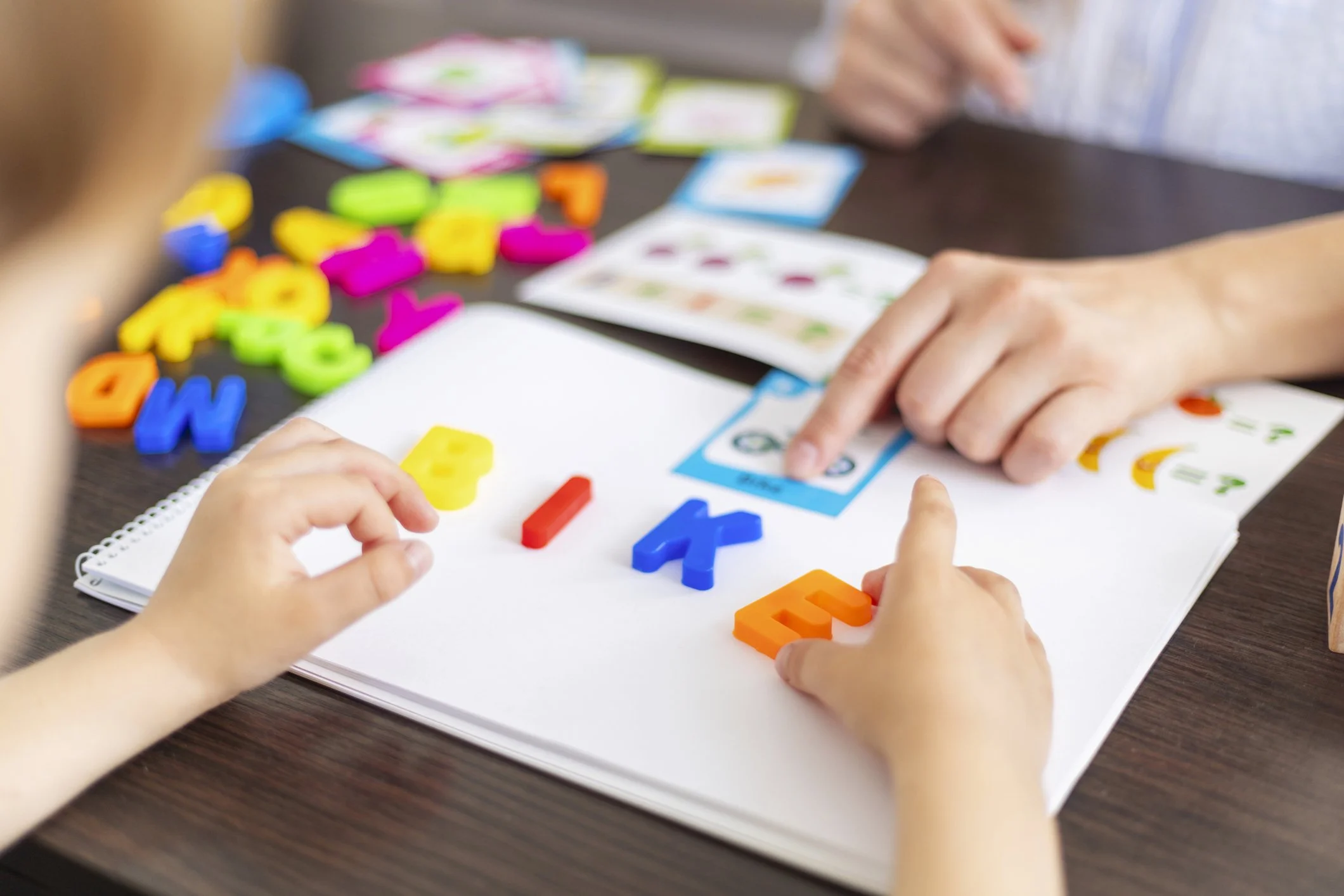 Children playing a colorful alphabet and money-themed educational game on a table.