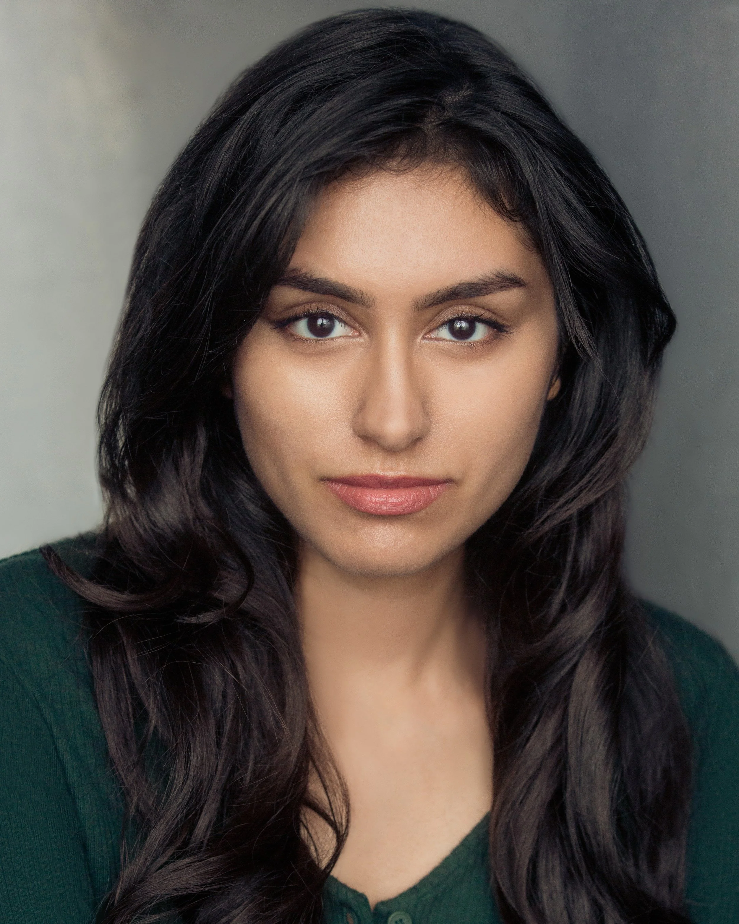 Close-up of a woman with dark hair and tan skin, wearing a dark green top, with only the upper part of her face visible.