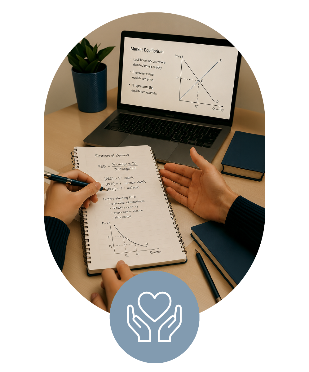 A student being tutored on A level economics with notes on demand elasticity and a graph on market equilibrium on a spiral notebook and laptop on a wooden desk, with a potted plant and stacked books.