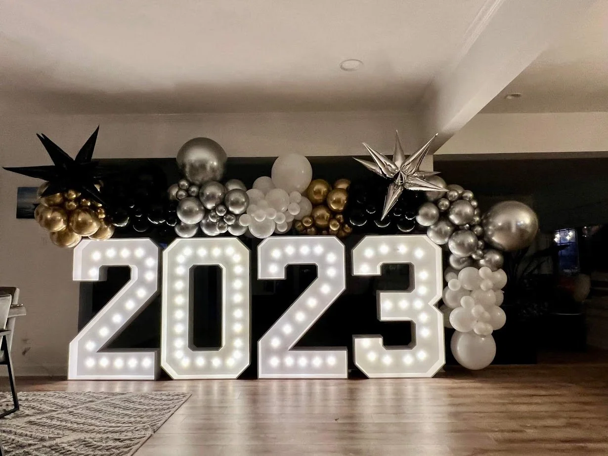 Large illuminated numbers reading 2023 surrounded by silver, white, black, and gold balloons in a festive New Years Eve display.