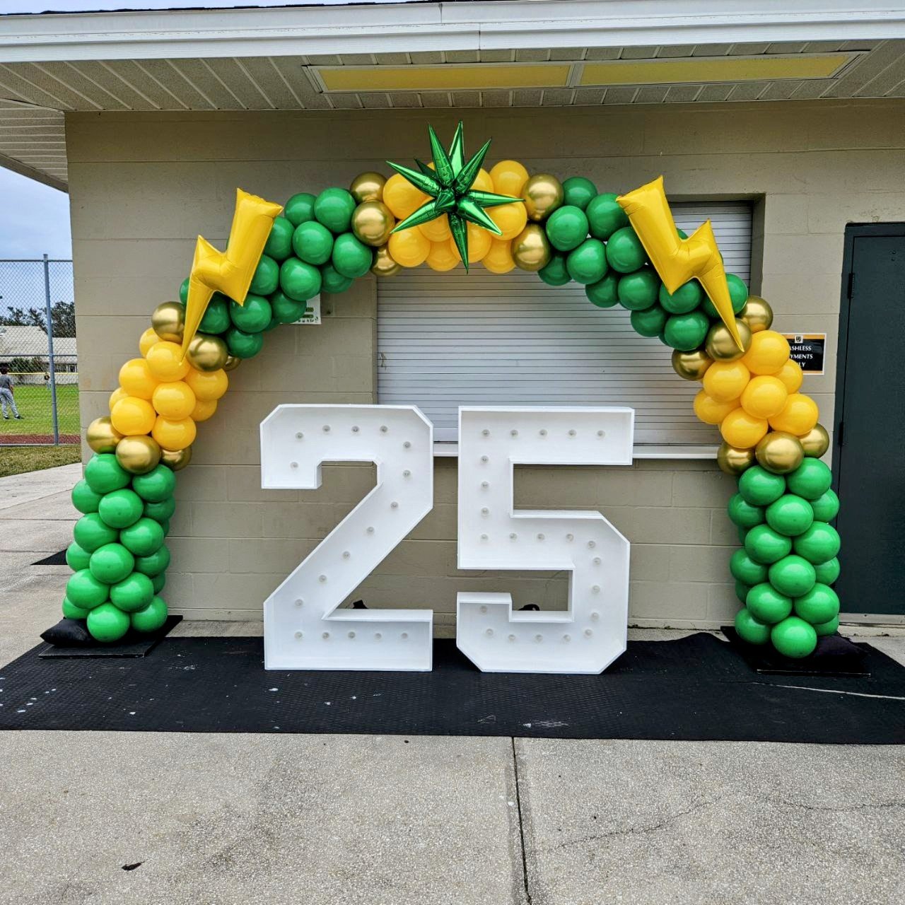 GREEN AND GOLDEN YELLOW BALLOON ARCH SURROUNDING 25 NUMBER MARQUEES