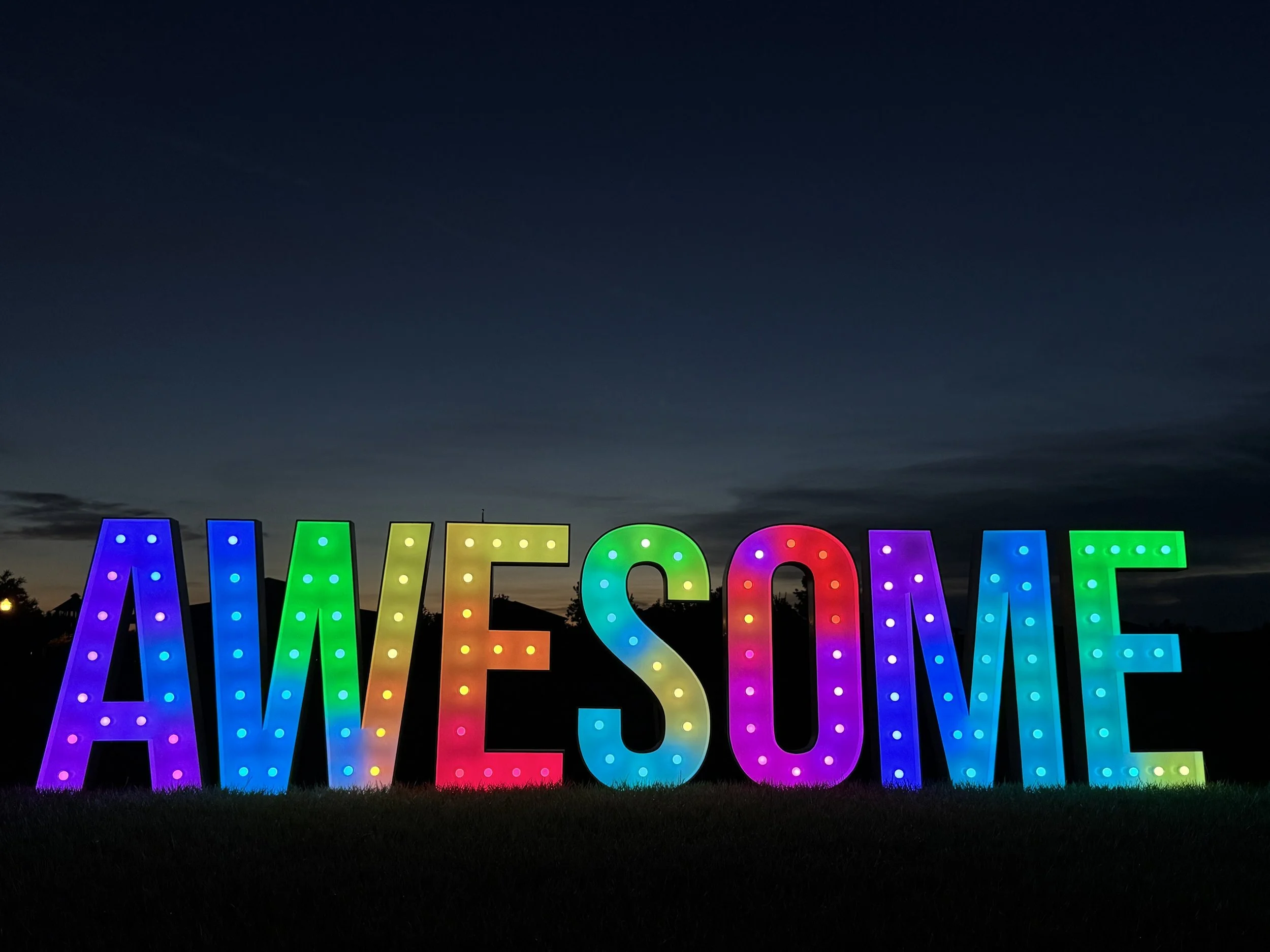 Colorful 5 FT tall LED-lit letters spelling out 'AWESOME' with a dark evening sky background.