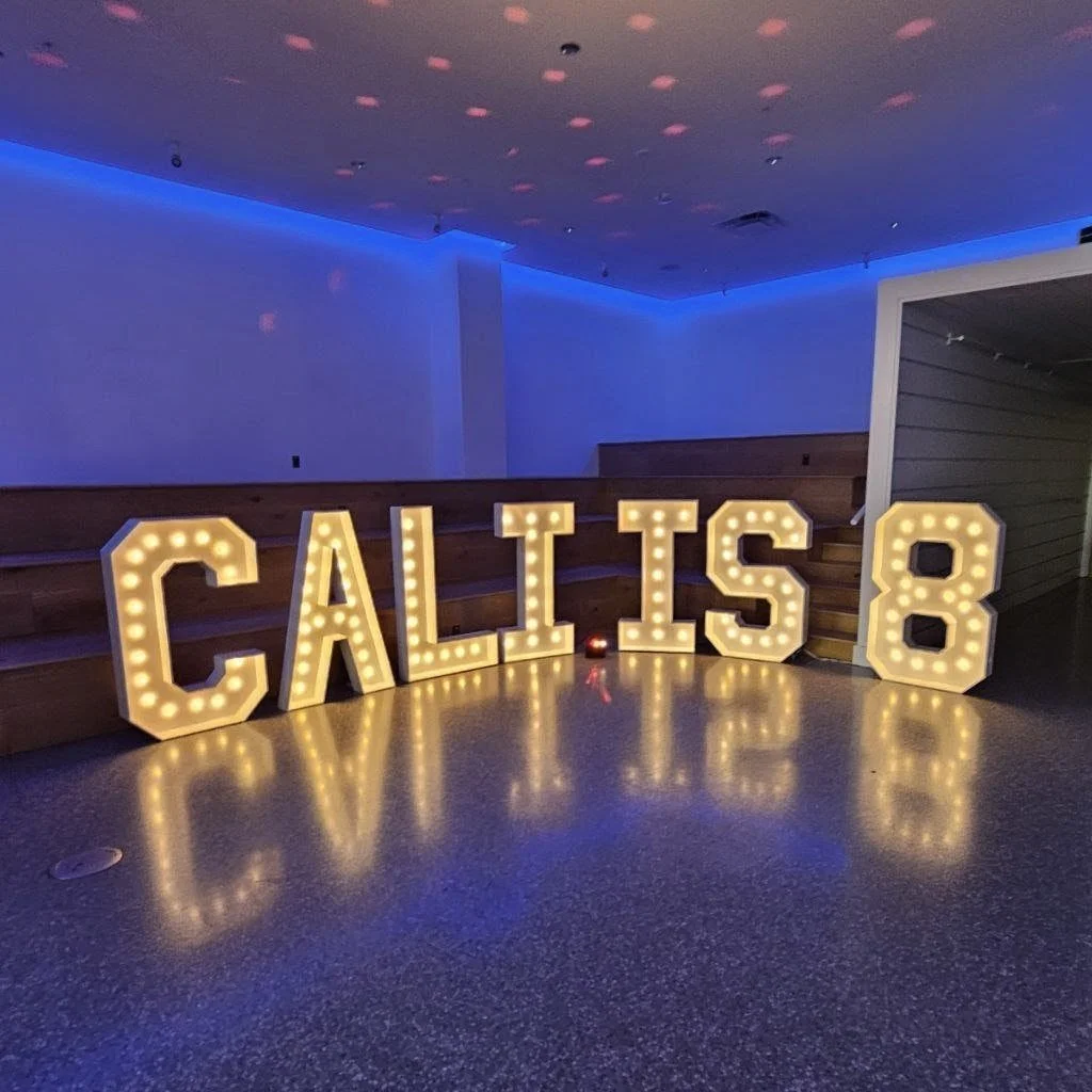 Large four ft illuminated marquee letters spell out 'CALI IS 8' in a room with blue ambient lighting. Birthday Party decorations
