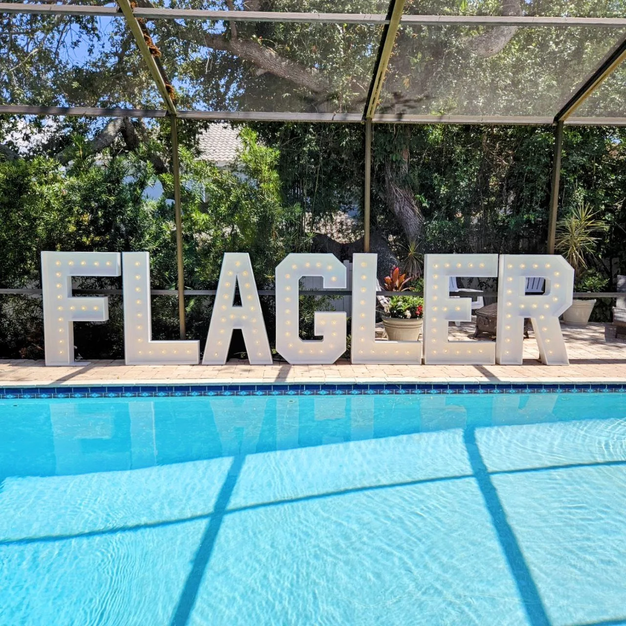 Large illuminated letters spelling 'FLAGLER' near a swimming pool. College School Name Sign