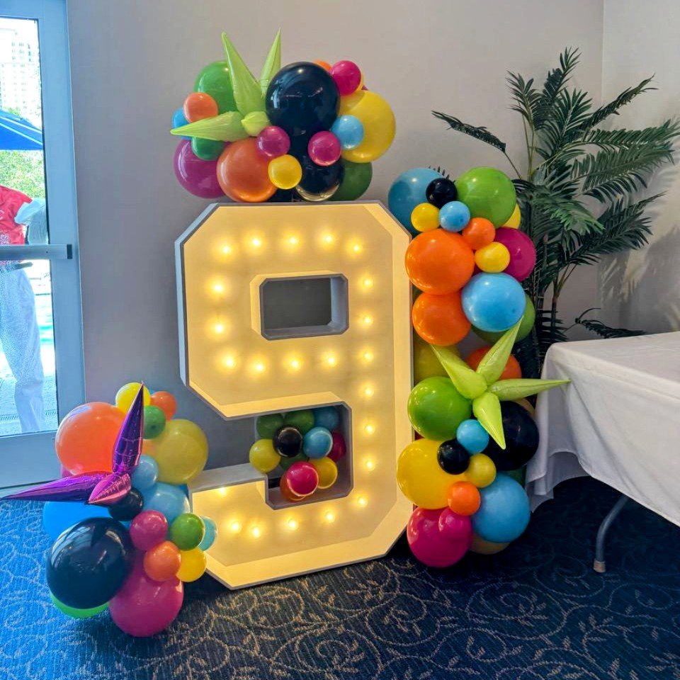 Decorative birthday display with a large lighted number nine, surrounded by colorful balloons and inflatable star-shaped balloons.