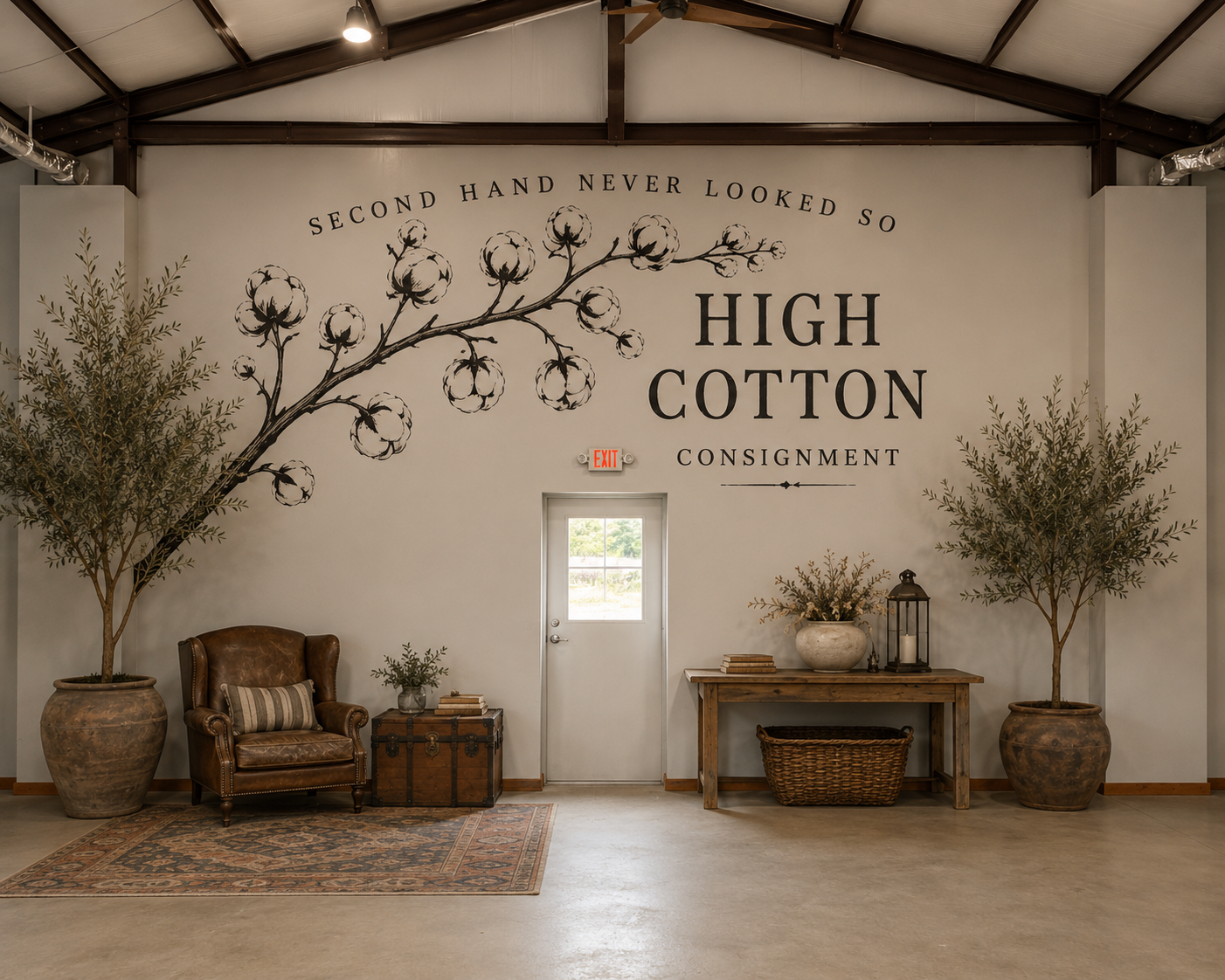 Interior of a rustic-style building with a large wall display featuring cotton plant illustrations and text that says, 'Second hand never looked so high cotton consignment.' There are two large potted trees on either side, a leather armchair with a pillow, a vintage chest, a wooden table with decorative items, and a small window with an exit sign above it.