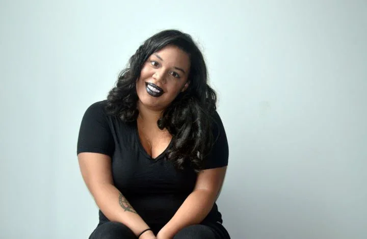 Photo of a light skin Black women with long hair and a black shirt, facing the camera