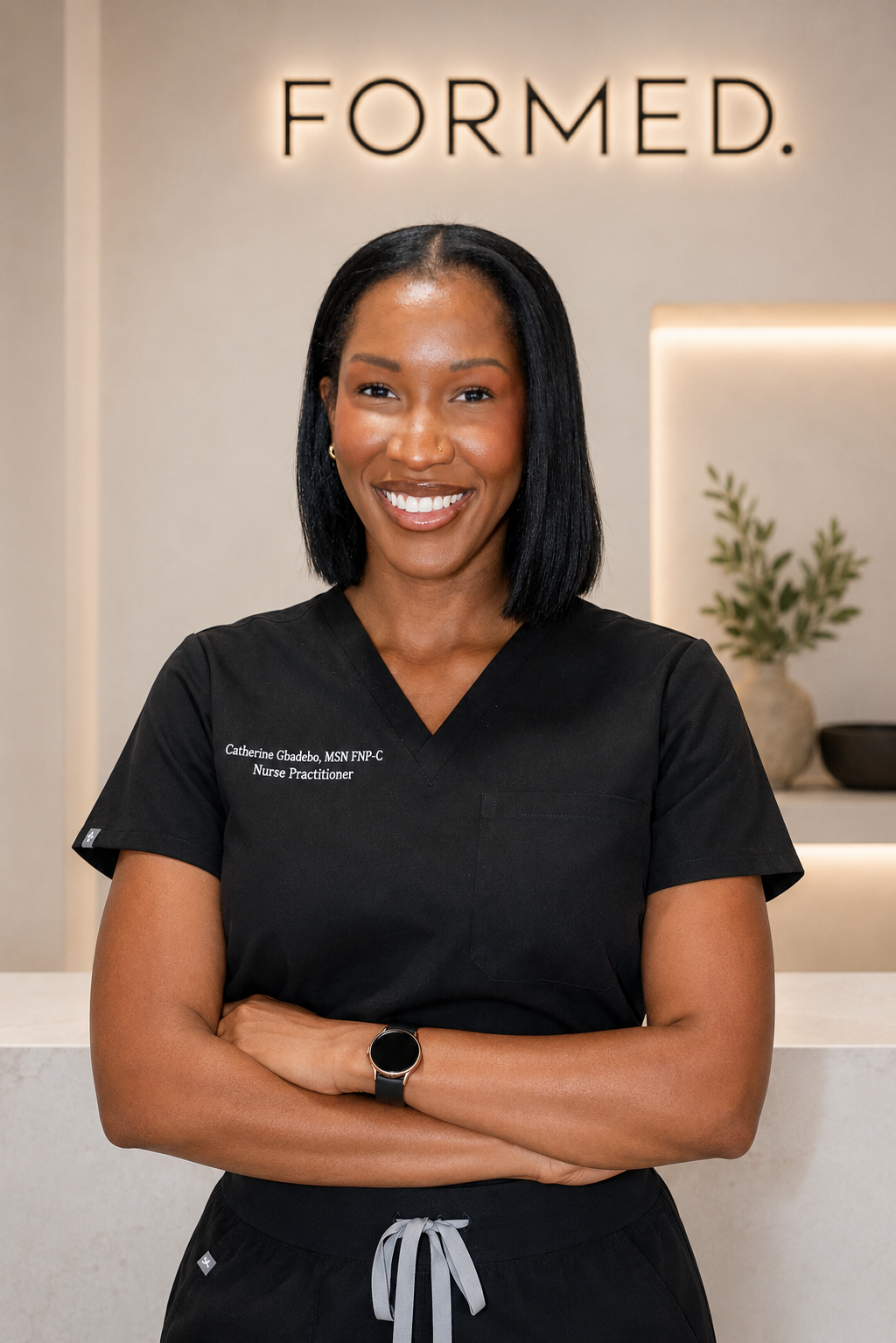 A smiling African American woman wearing black medical scrubs standing with arms crossed in a modern reception area with the word 'FORMED.' illuminated on the wall behind her.