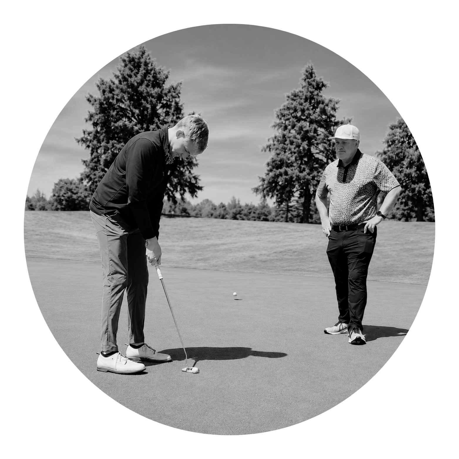 Black and white photo of golf players on the green, one preparing to putt, the other observing, with trees in the background.