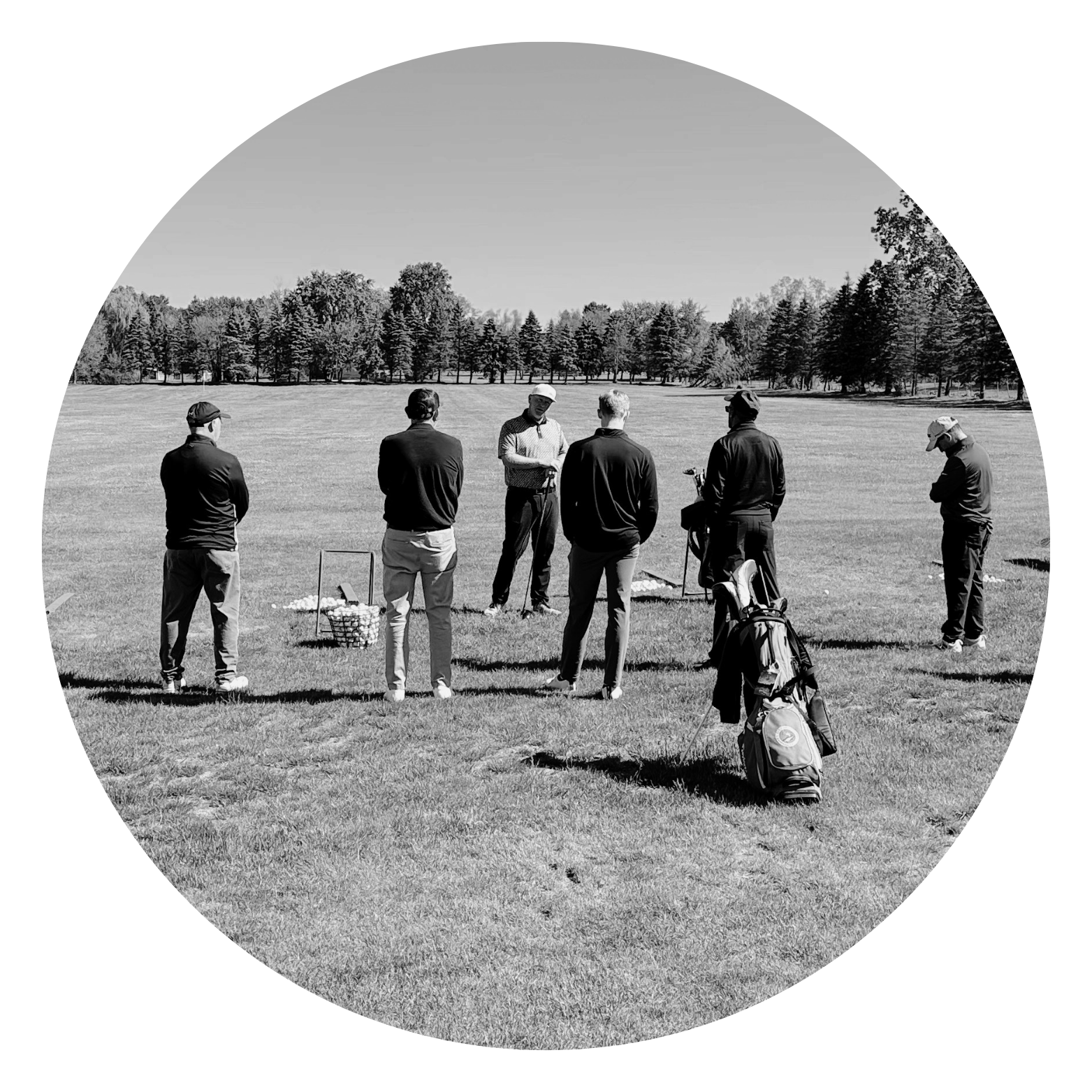 A group of six men standing on a golf course, some with golf clubs and golf bags, with trees in the background, and one man appears to be giving instructions or a lesson.