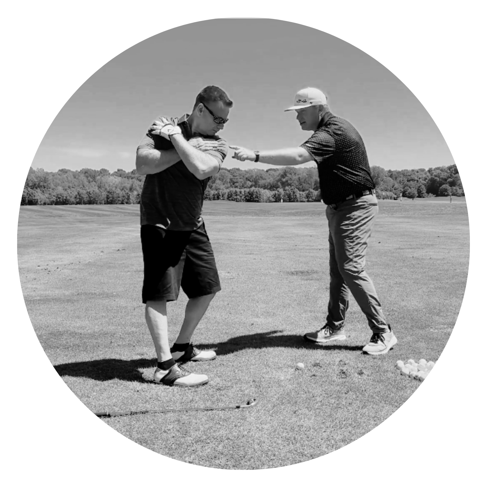 Two men on a golf course, one near the ground and the other pointing, with golf balls on the grass.