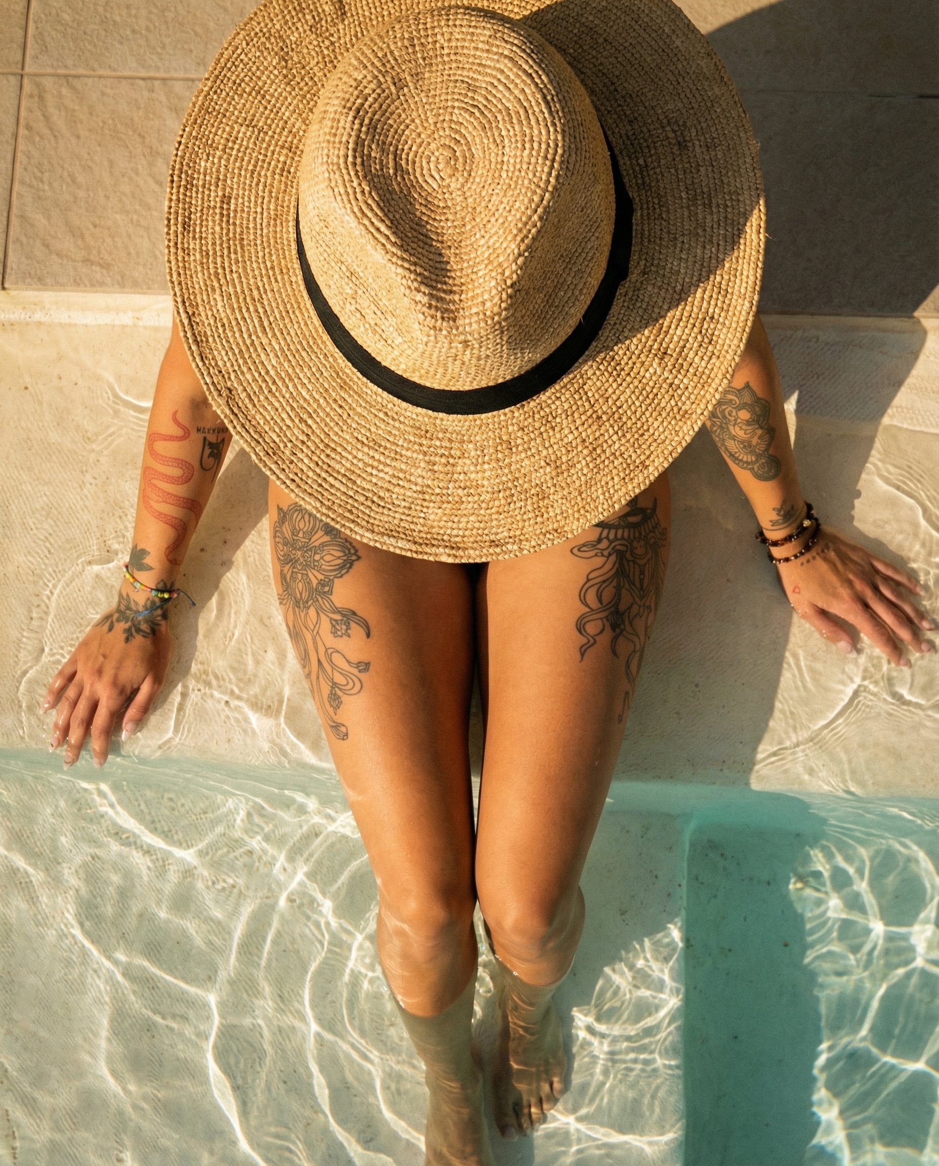 Frau mit Tattoos, Sonnenhut und Schmuck entspannt im Wasser liegend, Nahaufnahme