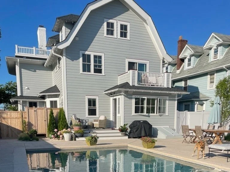 Backyard with a pool, outdoor seating area, and a three-story gray house with a unique roof design