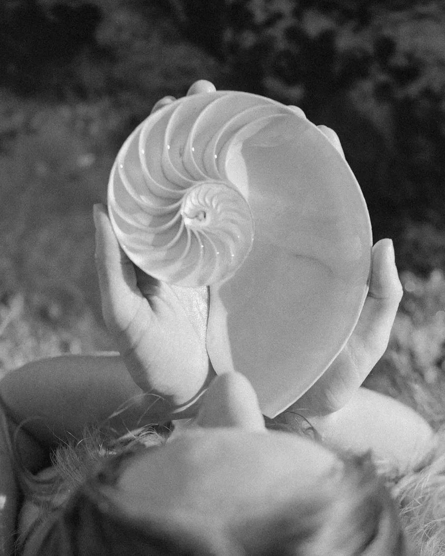 A person holding a seashell-shaped object with a spiral design, black and white photo.