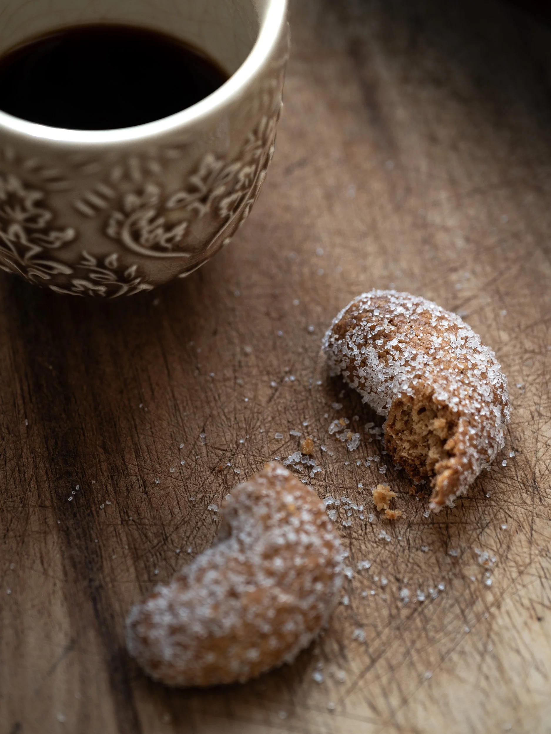 Tazza di caffè nero e dolcetti ricoperti di zucchero di canna su un tagliere di legno.