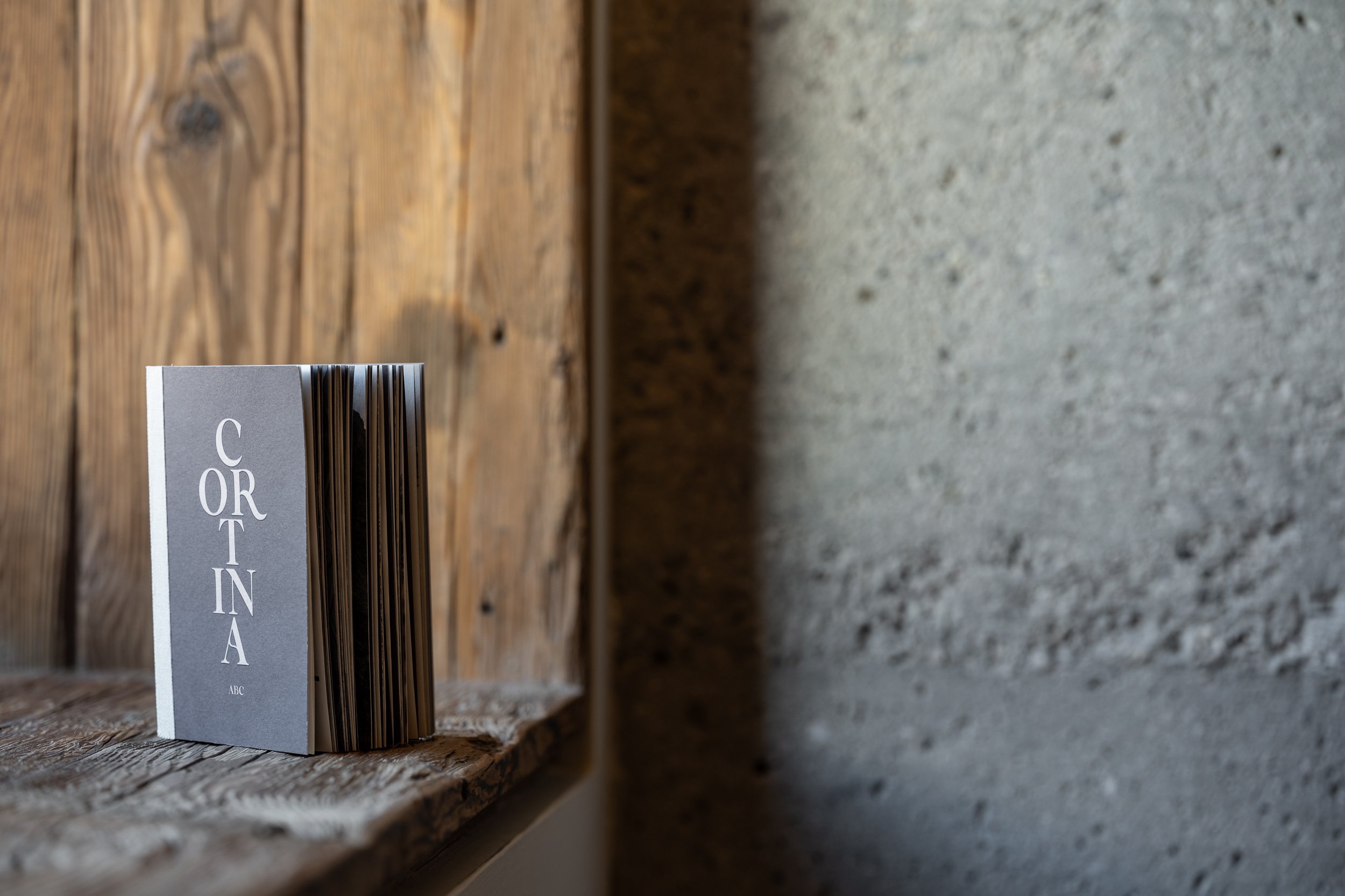Un catalogo con la scritta 'CONTINA' appoggiato su una superficie di legno di fronte a un muro di pietra Grey.