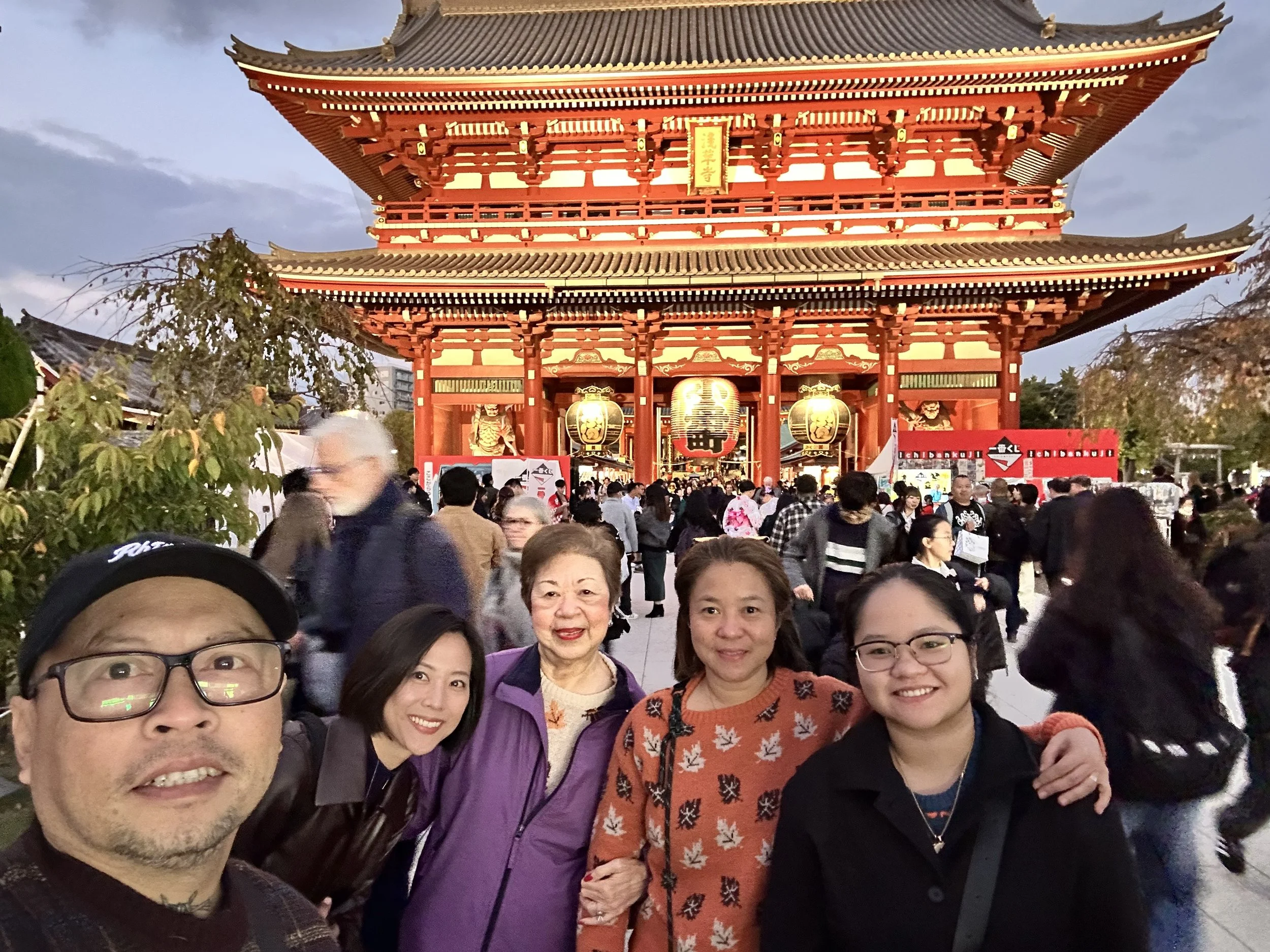 A group of people taking a selfie in front of a traditional Japanese temple gate at night.