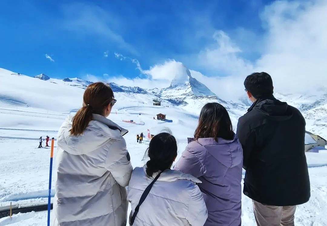Group of four people in winter clothing watching snow-covered mountains and Matterhorn peak in the distance