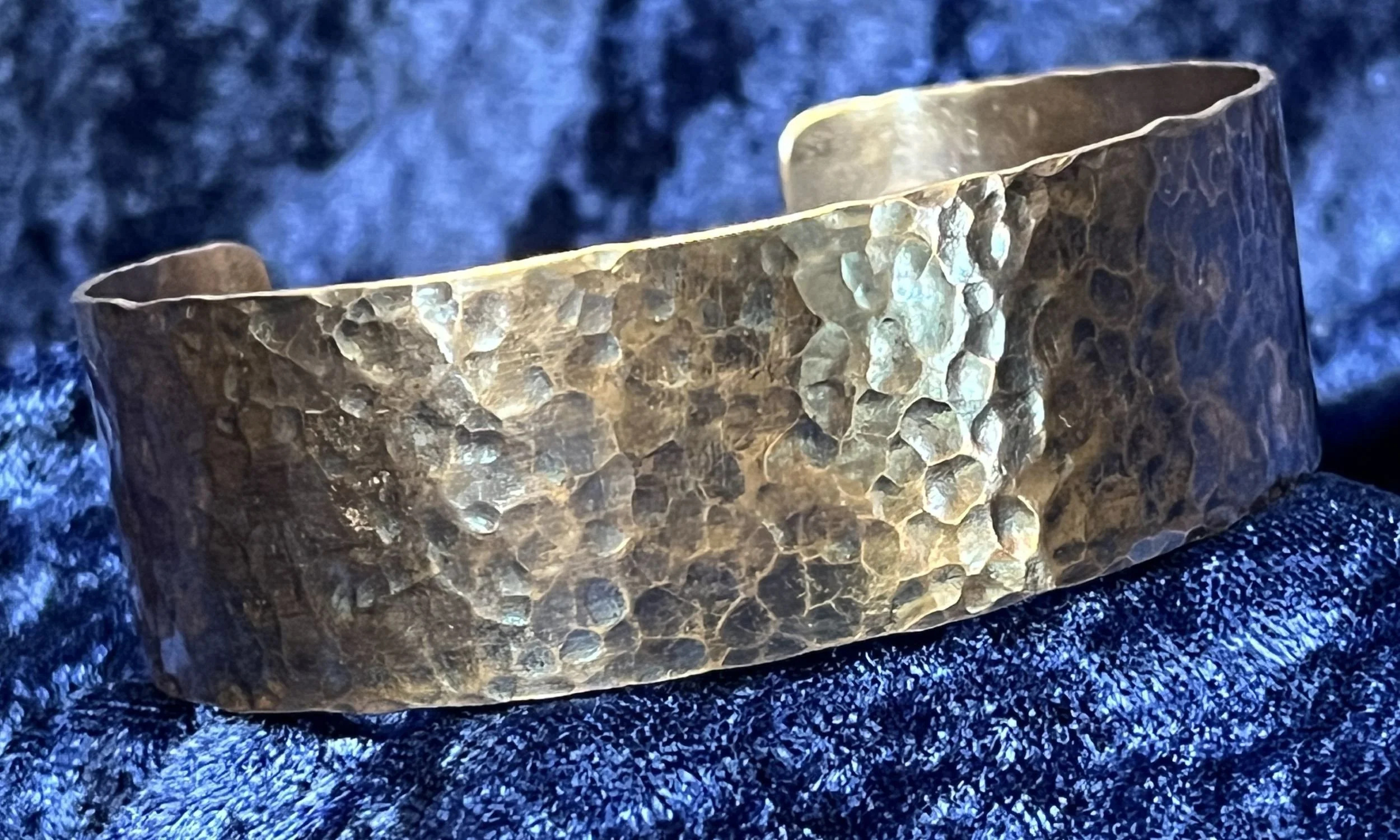 Hammered Copper bracelet laying on a blue background.