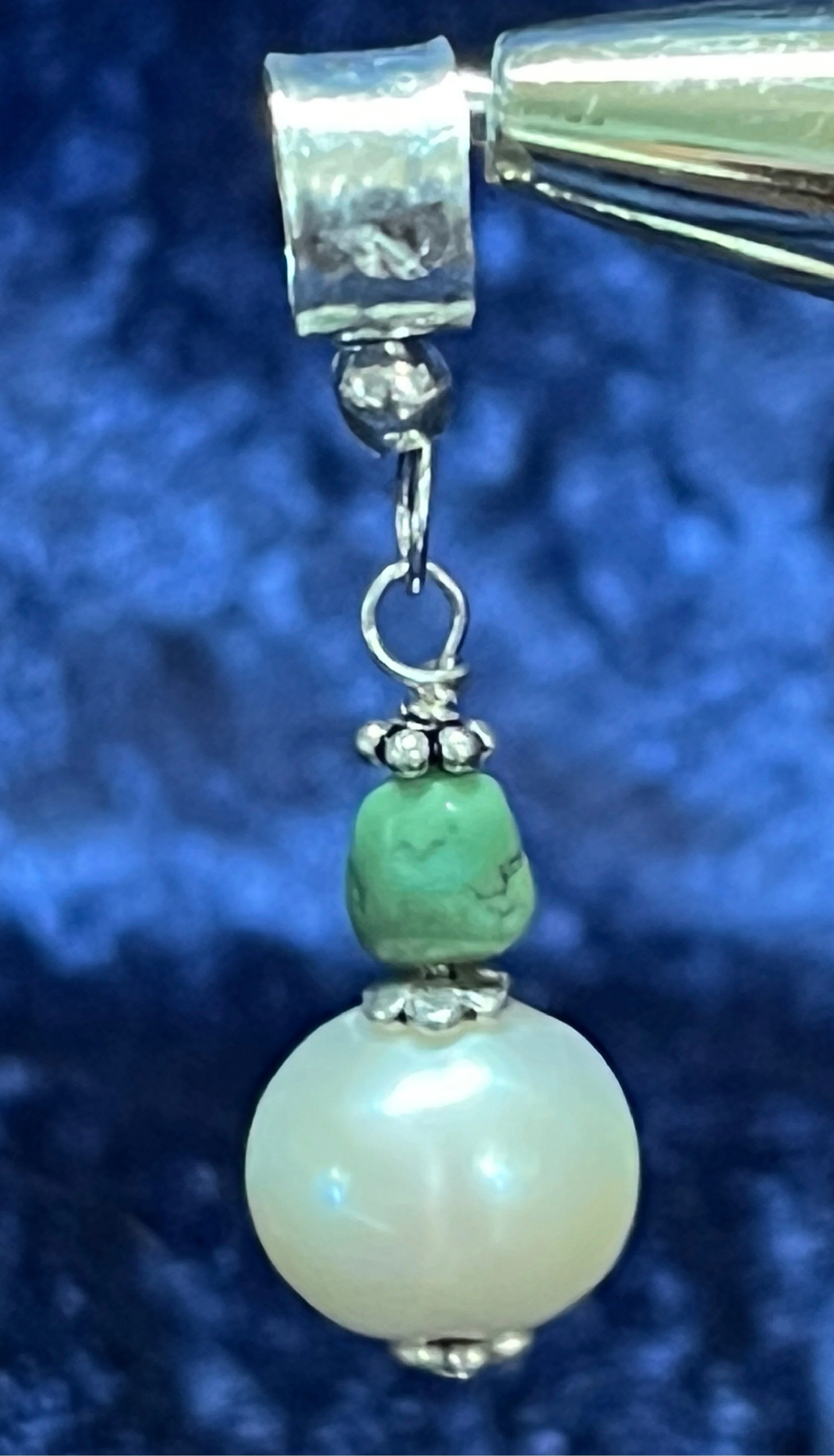 Pearl and turquoise charm hanging on blue background.